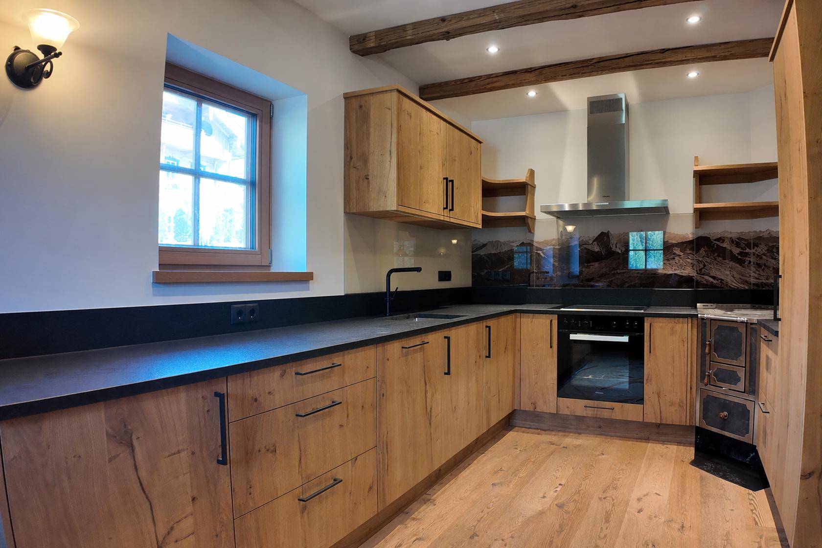 Moderne Holzküche mit dunklen Arbeitsplatten, integrierten Geräten und traditionellem Holzofen.