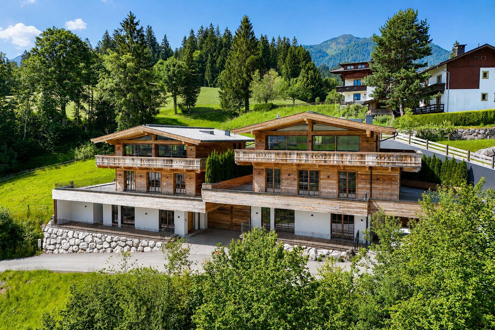 Zwei moderne Chalets in alpiner Landschaft mit grünen Hügeln und Bergblick.