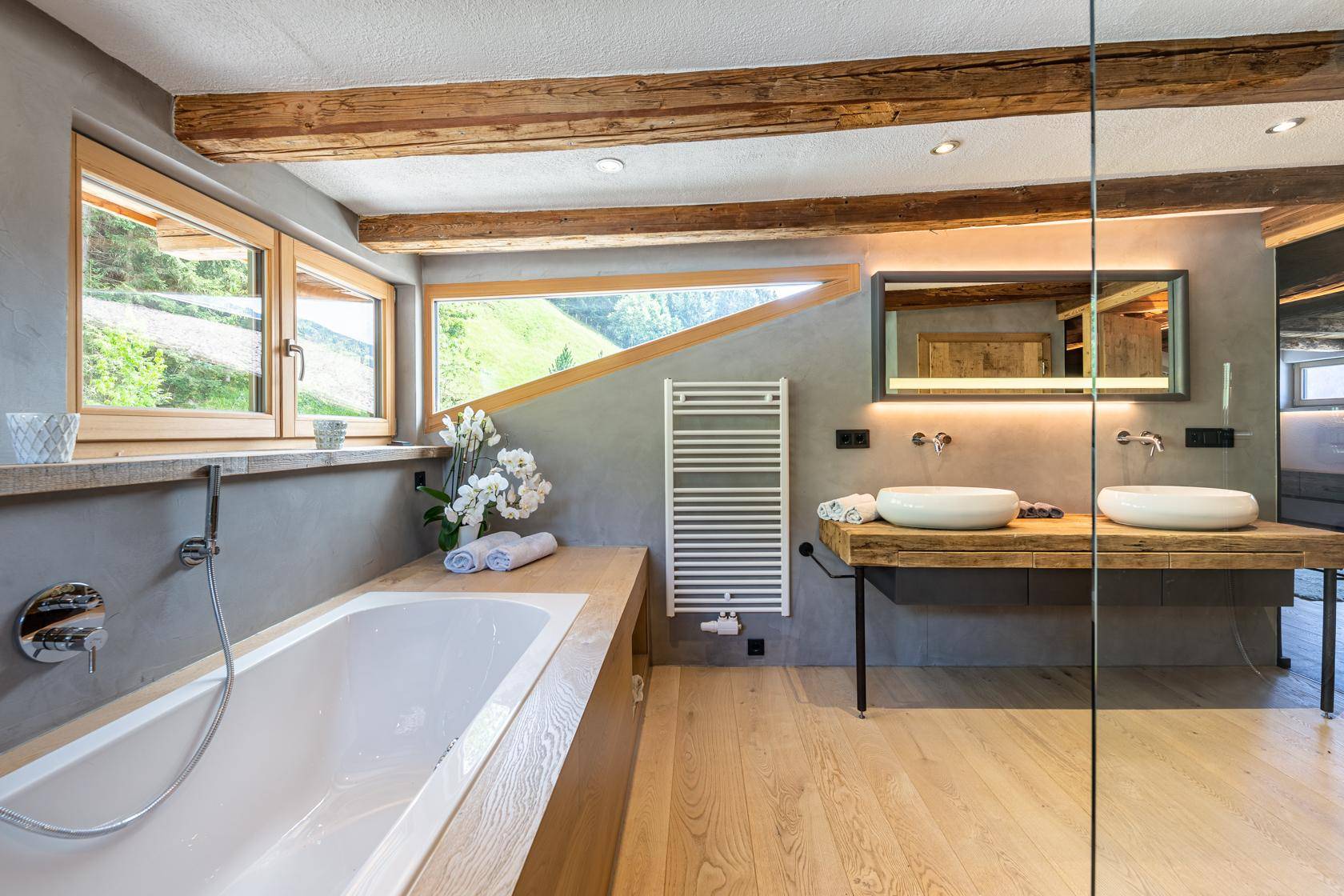 Modernes Badezimmer mit Holzboden, Doppelwaschbecken und Badewanne unter Schrägfenstern.