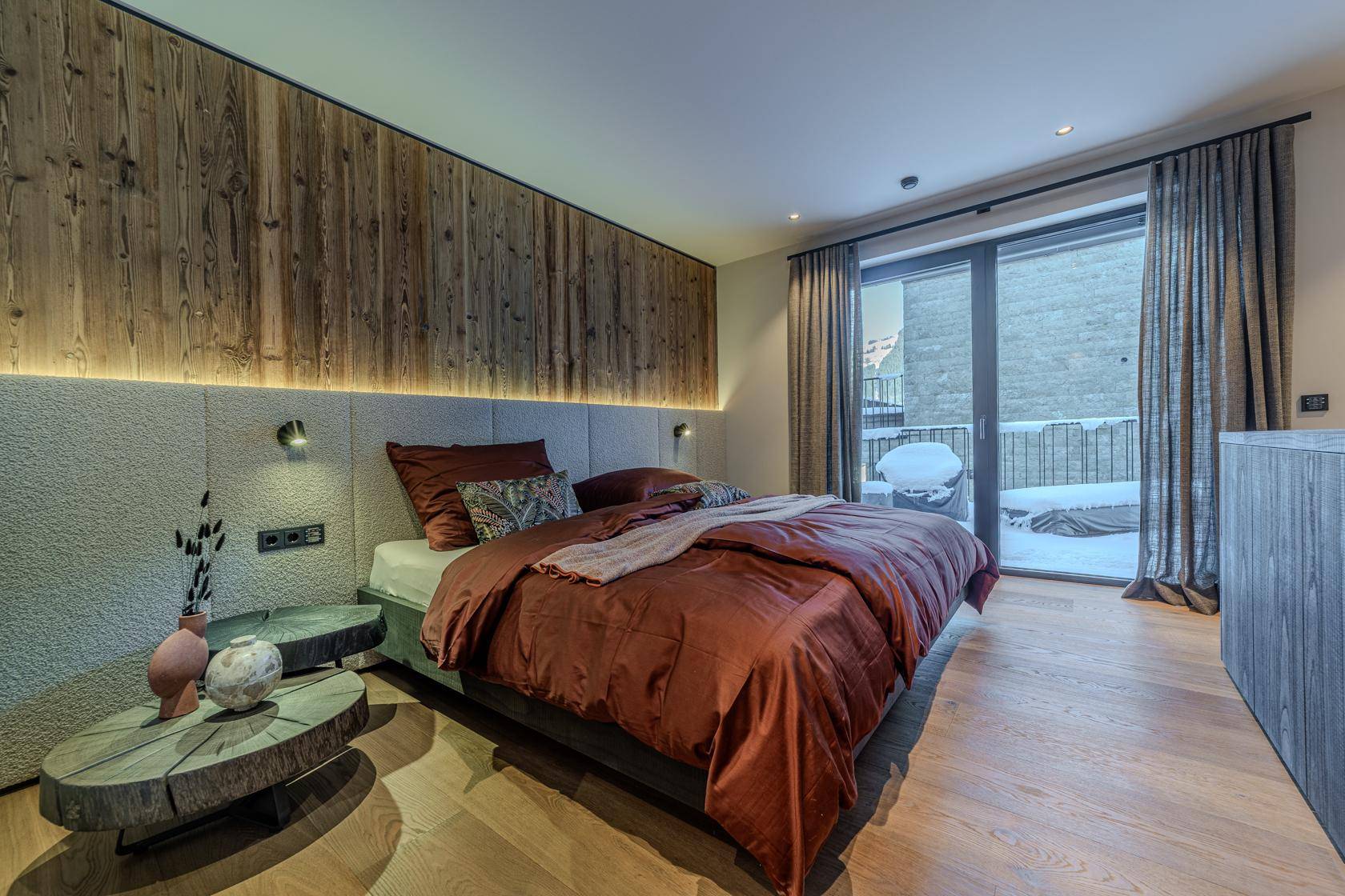 Gemütliches Schlafzimmer mit Holzwand, großem Bett und Zugang zu einem Balkon.