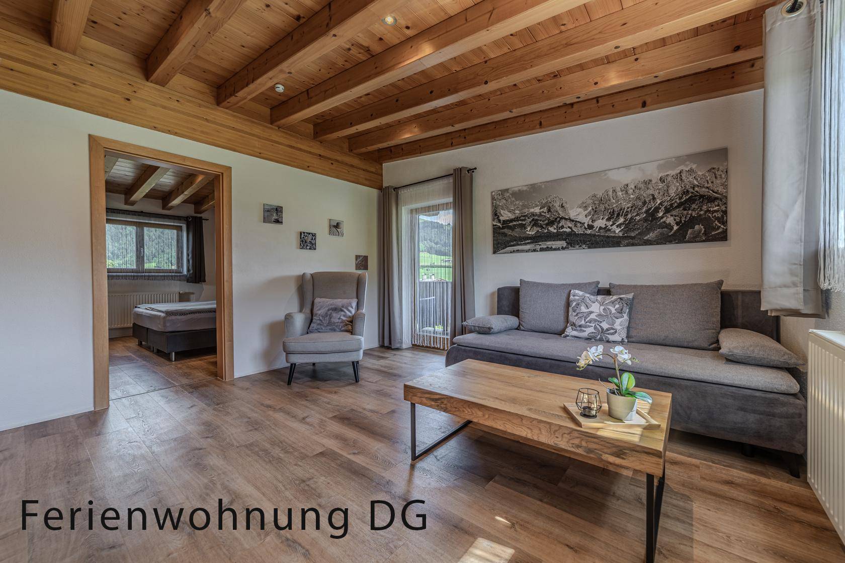 Rustikales Wohnzimmer mit Holzbalkendecke, Sofa und Zugang zu einem Balkon mit Bergblick.