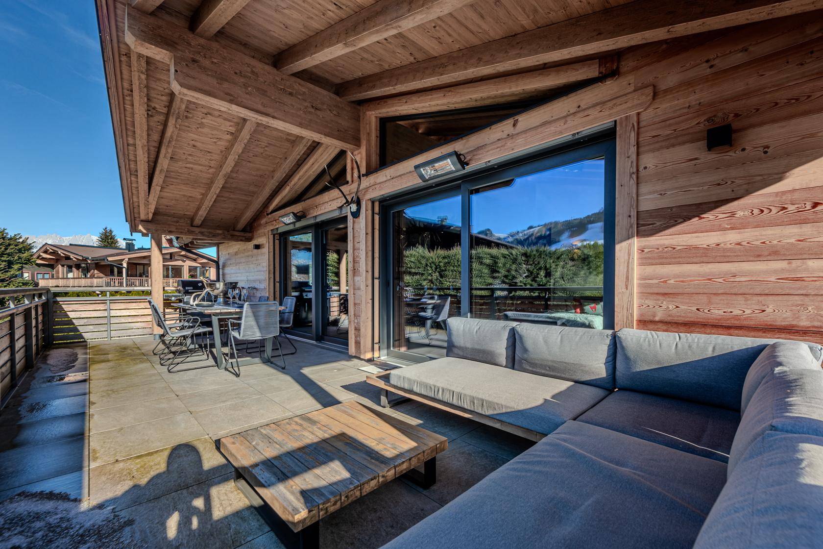 Große Sonnenterrasse mit Lounge-Möbeln und Esstisch, umgeben von Holzelementen und Bergblick.