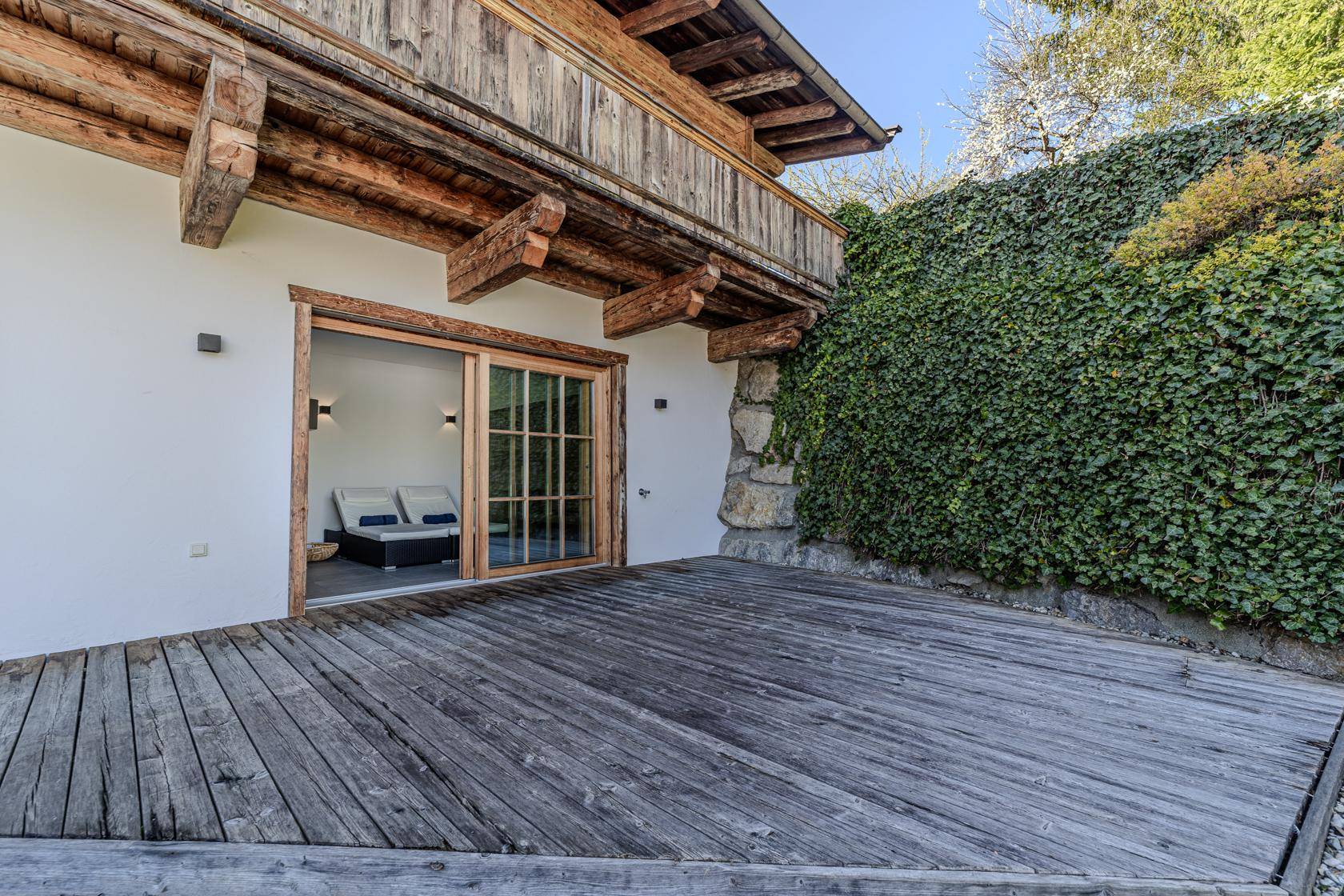 Private Holzterrasse mit direktem Zugang zum Wellnessbereich und grüner Wand.