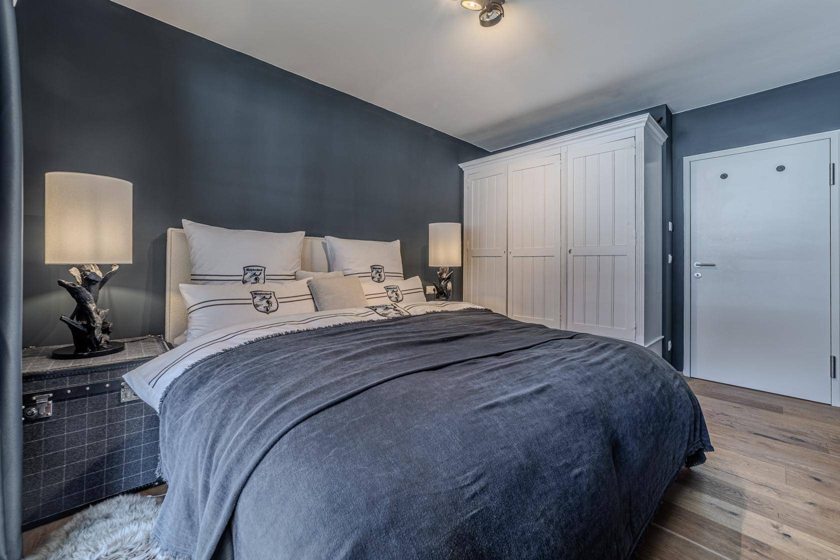 Schlafzimmer mit großem Bett, weißem Kleiderschrank und dunklen Wänden.