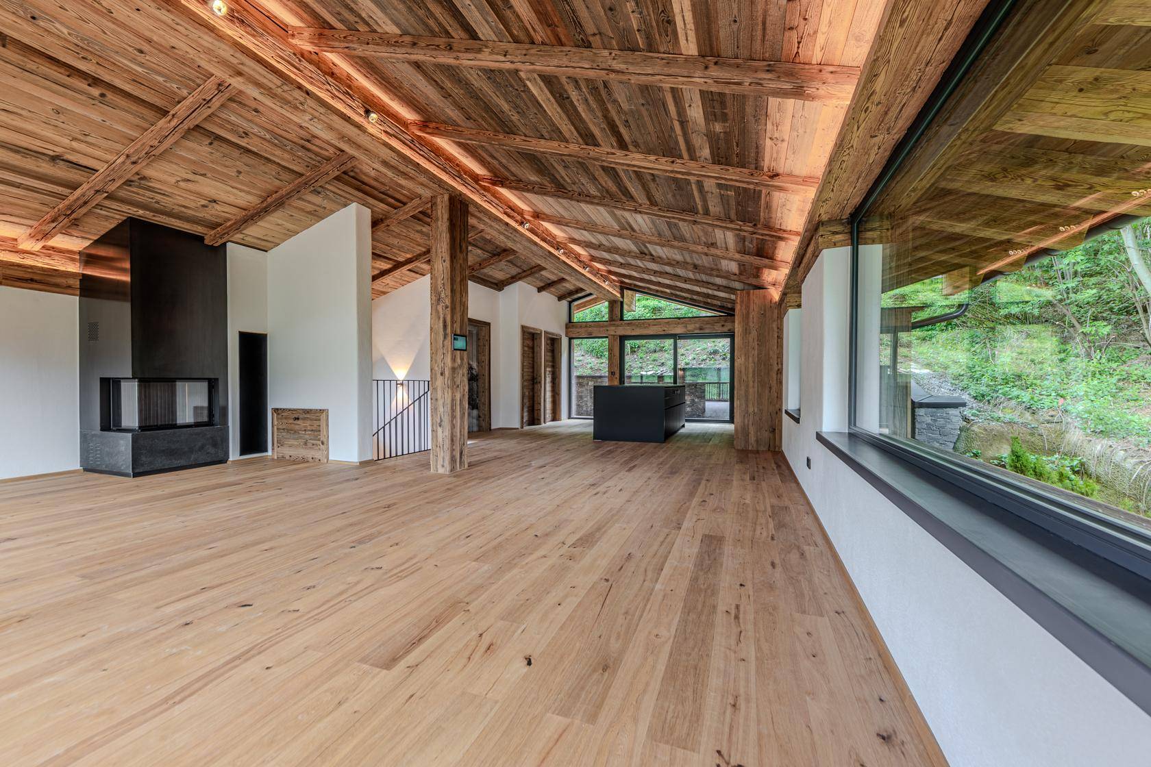Geräumiger Wohnbereich mit Holzbalkendecke, Kamin und großen Fenstern zur Natur.