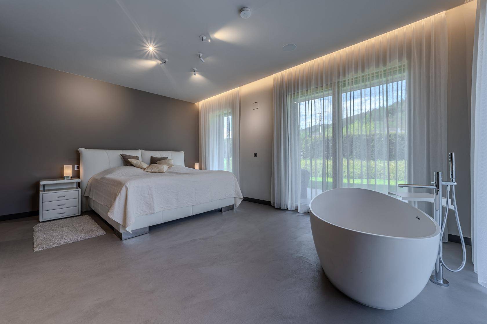 Geräumiges Schlafzimmer mit freistehender Badewanne und großen Fenstern zum Garten.