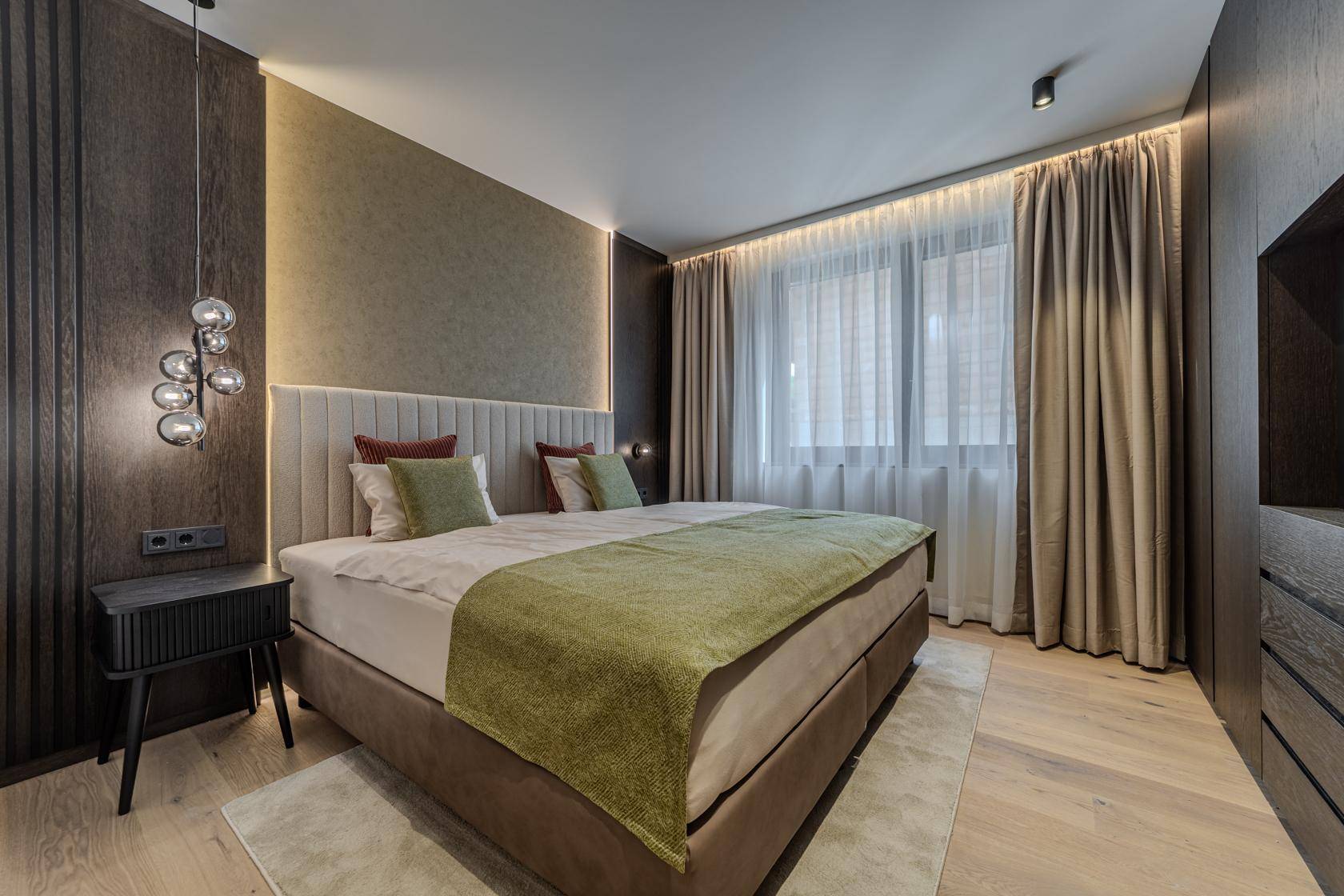 Gemütliches Schlafzimmer mit Doppelbett, Holzboden und großen Fenstern mit Vorhängen.