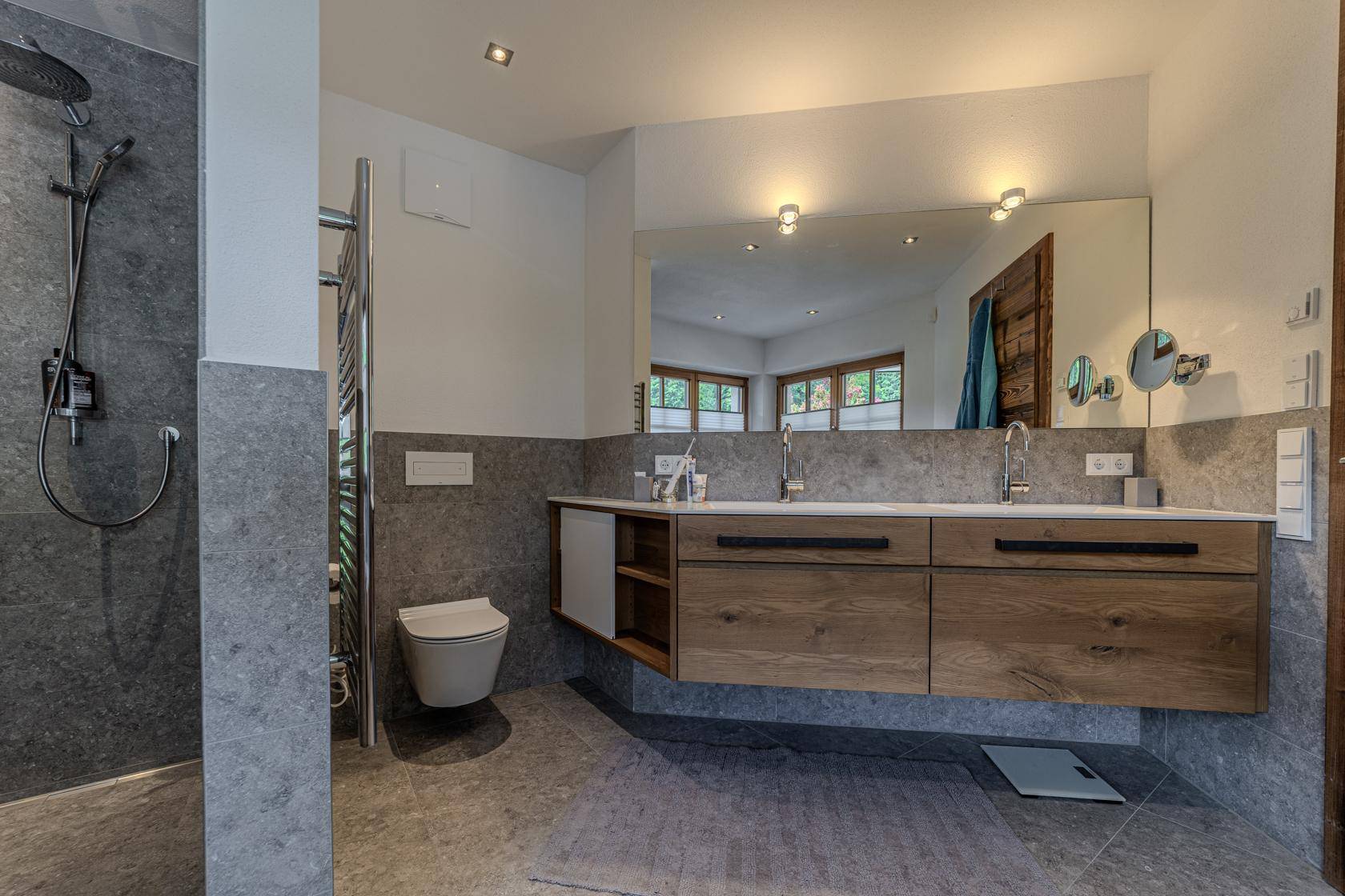 Modernes Badezimmer mit Doppelwaschbecken, begehbarer Dusche und Wand-WC.