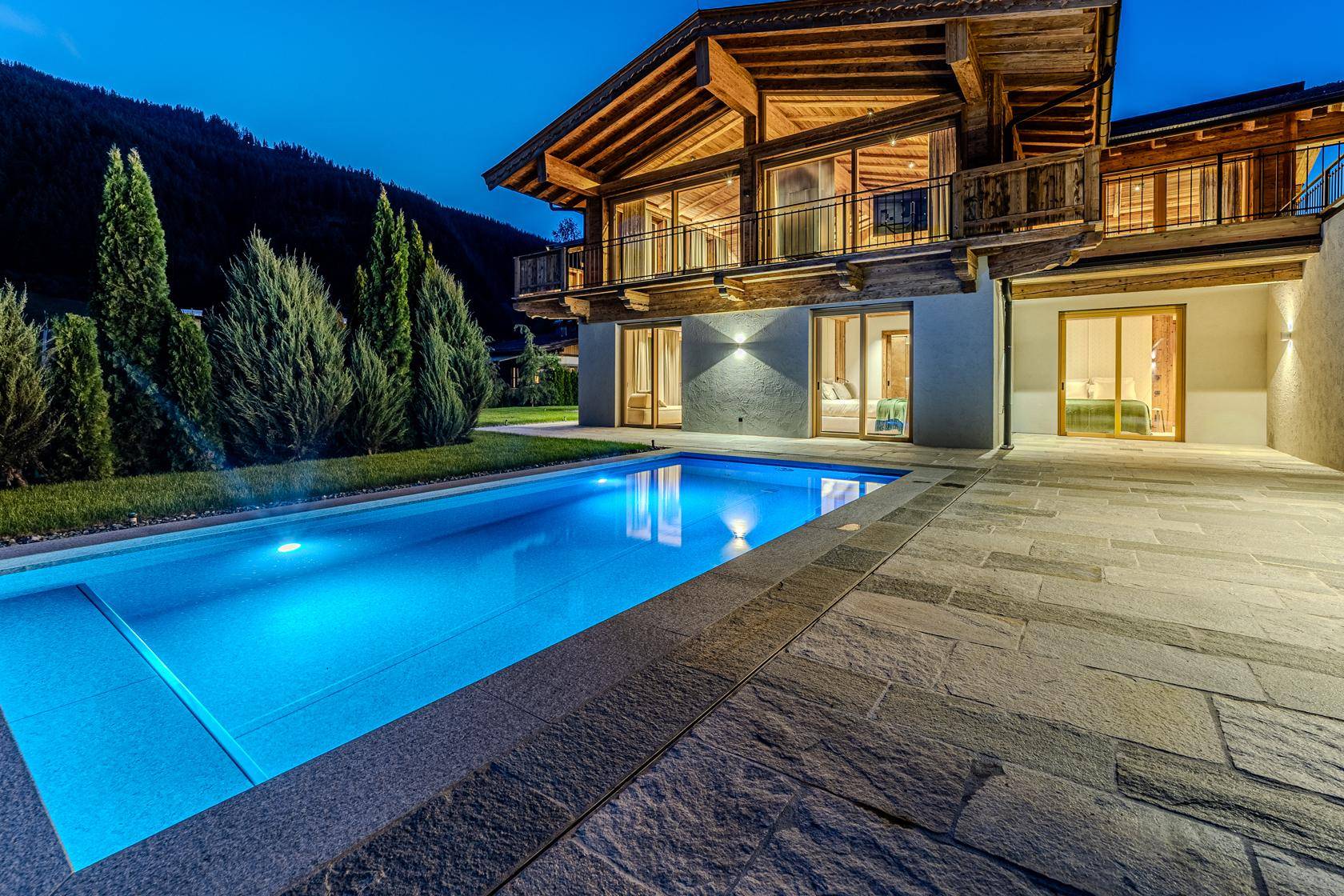 Stimmungsvolle Außenansicht des Chalets mit beleuchtetem Pool und Terrasse am Abend.
