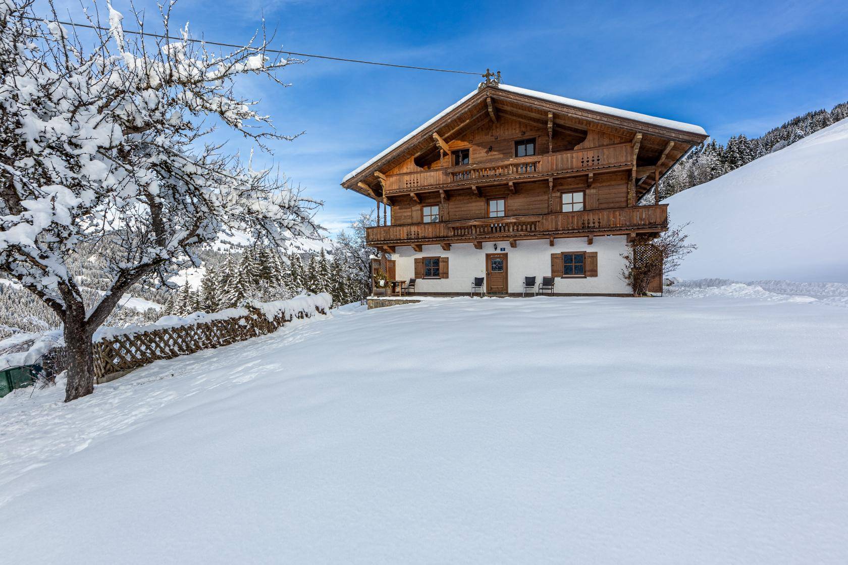 Traditionelles Holzhaus mit weißer Fassade und Holzbalkonen, umgeben von tiefem Schnee und Bergen.