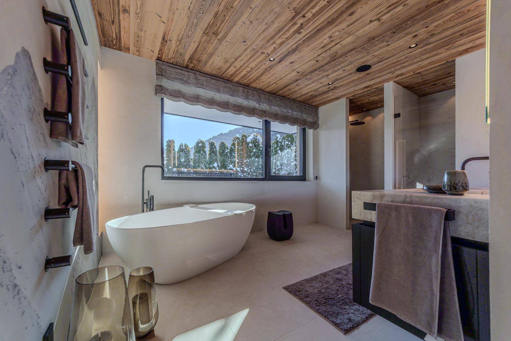 Helles Badezimmer mit freistehender Badewanne, großer Dusche und Fenster mit Bergblick.