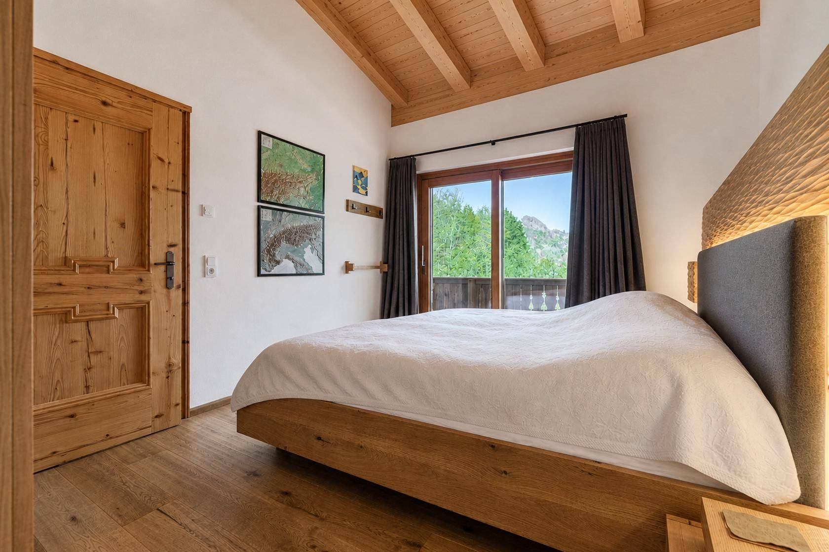 Gemütliches Schlafzimmer mit Holzbalkendecke, Holztür und Zugang zu einem Balkon.
