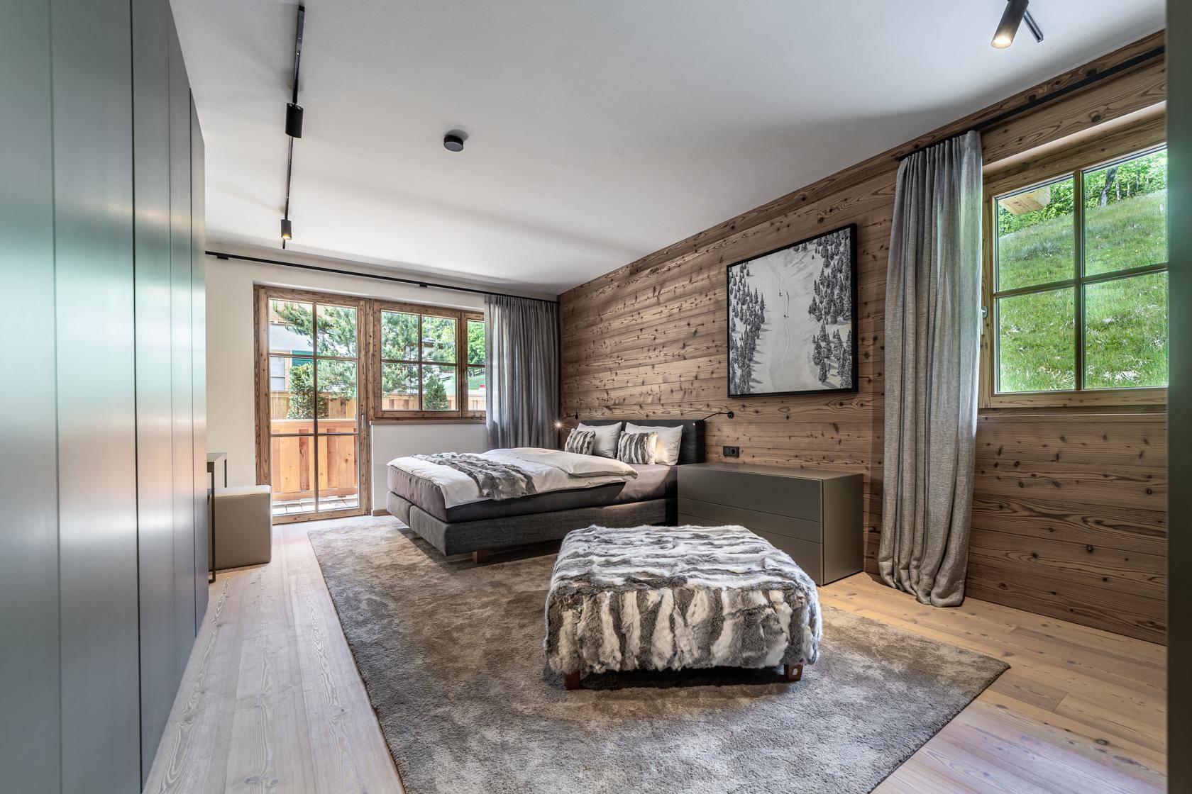 Gemütliches Schlafzimmer mit Holzwand, großem Bett und Zugang zu einem Balkon mit Bergblick.