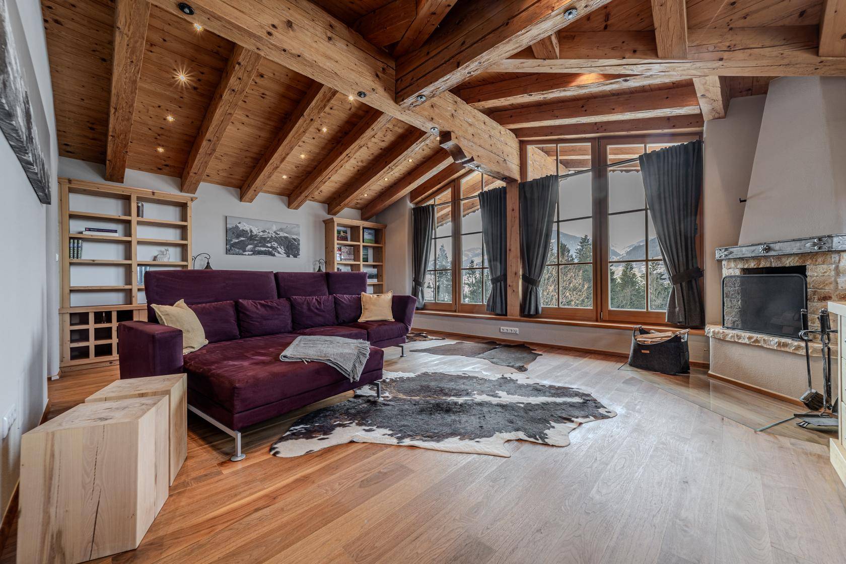 Geräumiges Wohnzimmer mit lila Sofa, eingebauten Regalen, Kamin und Holzbalkendecke.