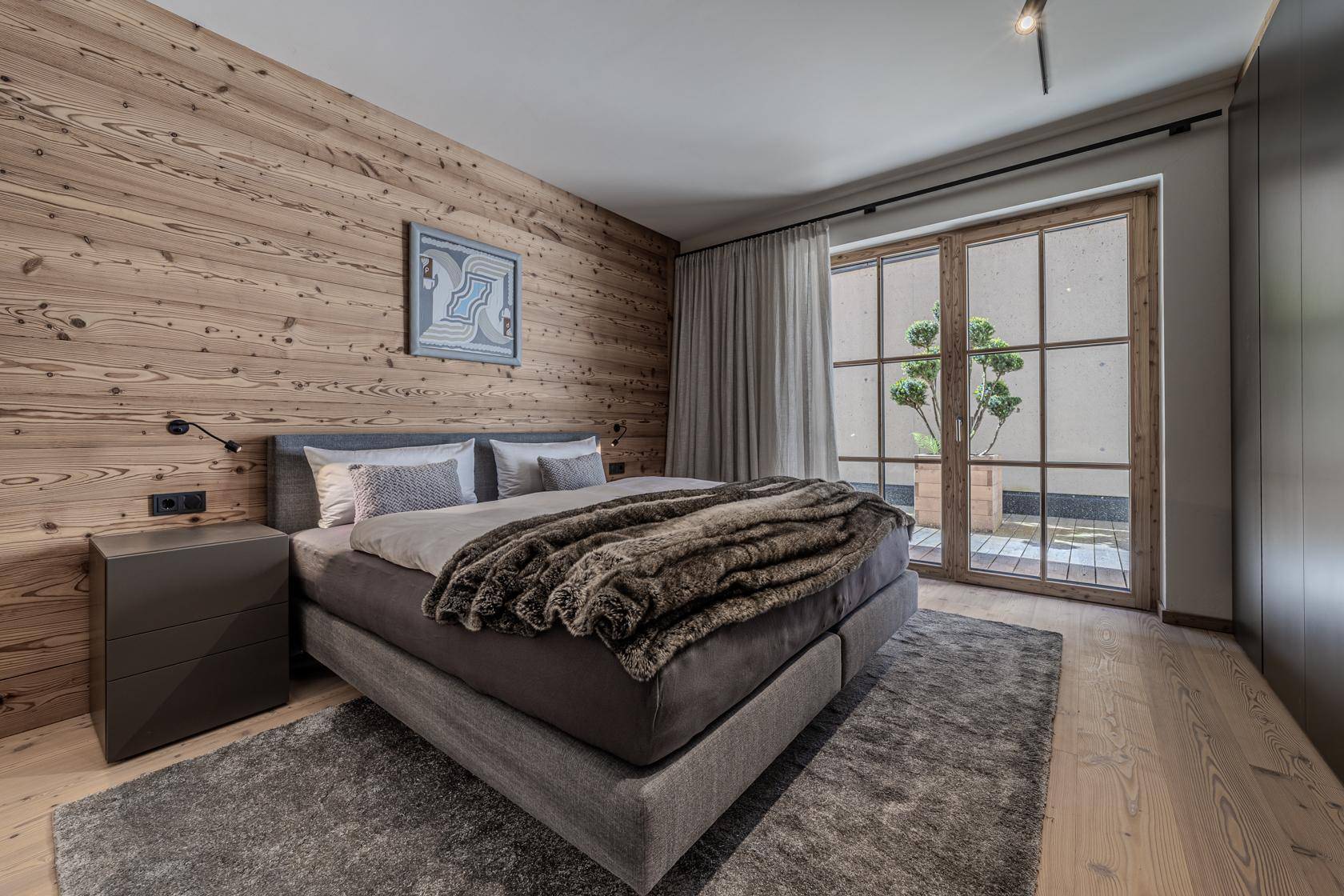 Komfortables Schlafzimmer mit Holzwand, weichem Teppich und Zugang zu einem privaten Außenbereich.
