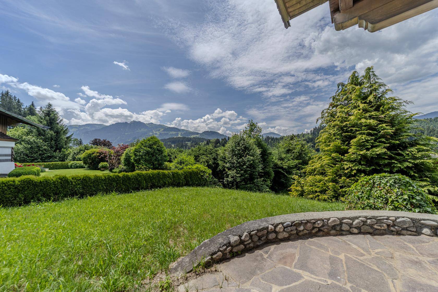 Sonniger Gartenbereich mit Steinterrasse und weitem Blick auf die umliegende Berglandschaft.