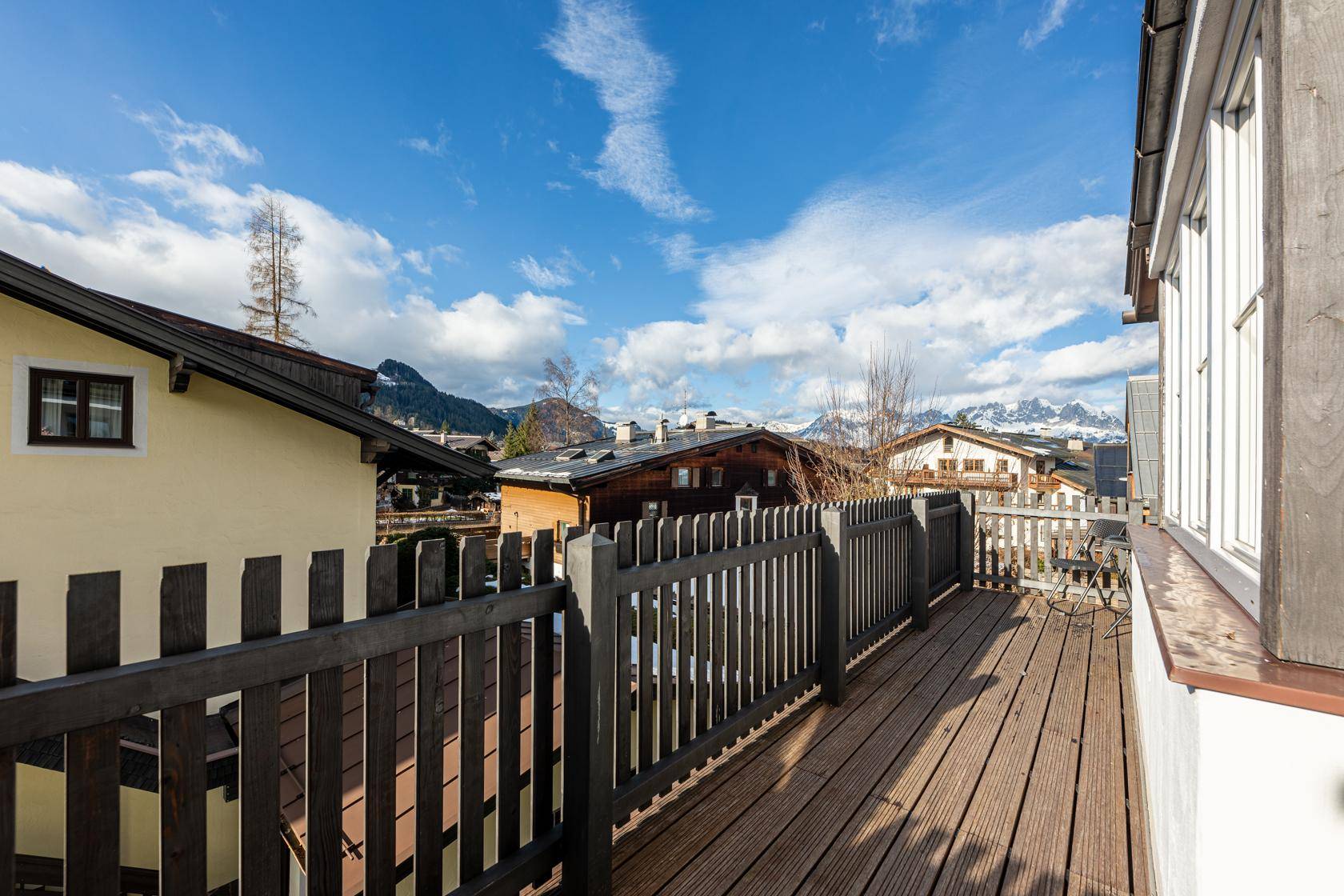 Langer Balkon mit Holzboden und Zaun, bietet einen weiten Blick auf die umliegende Berglandschaft.