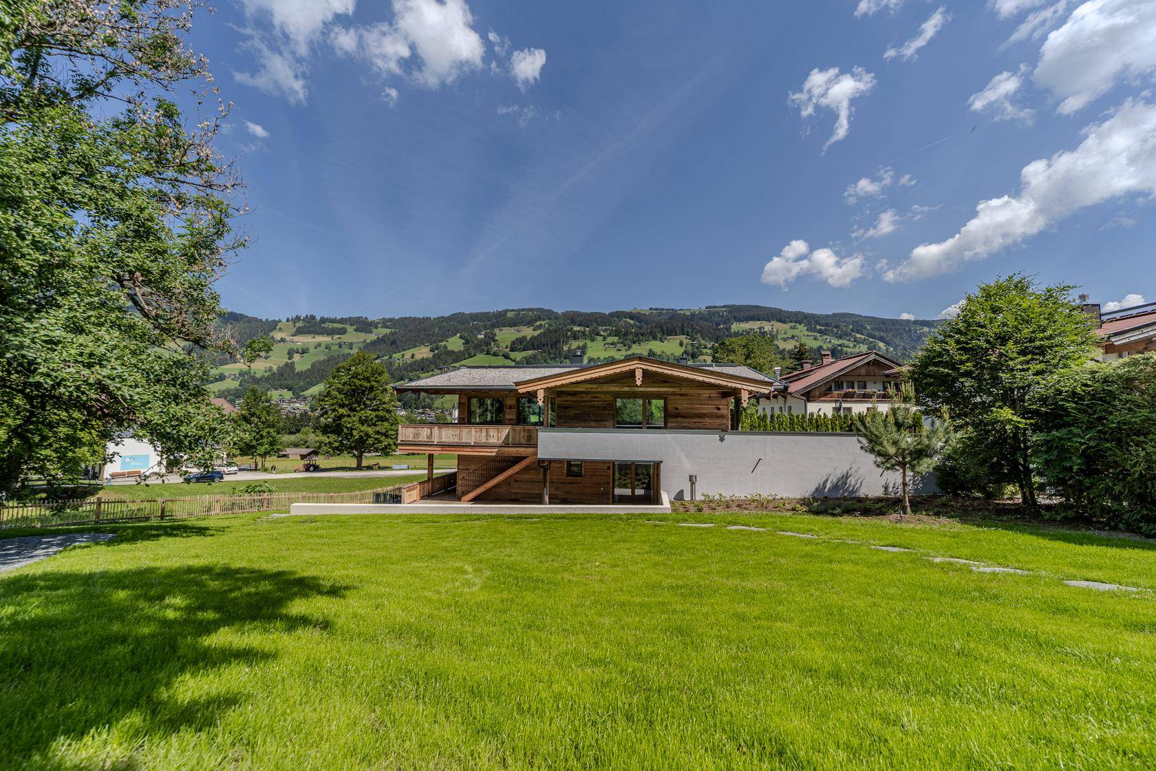 Freistehendes Holzhaus im Grünen mit weitläufigem Rasen und Bergblick an einem sonnigen Tag.
