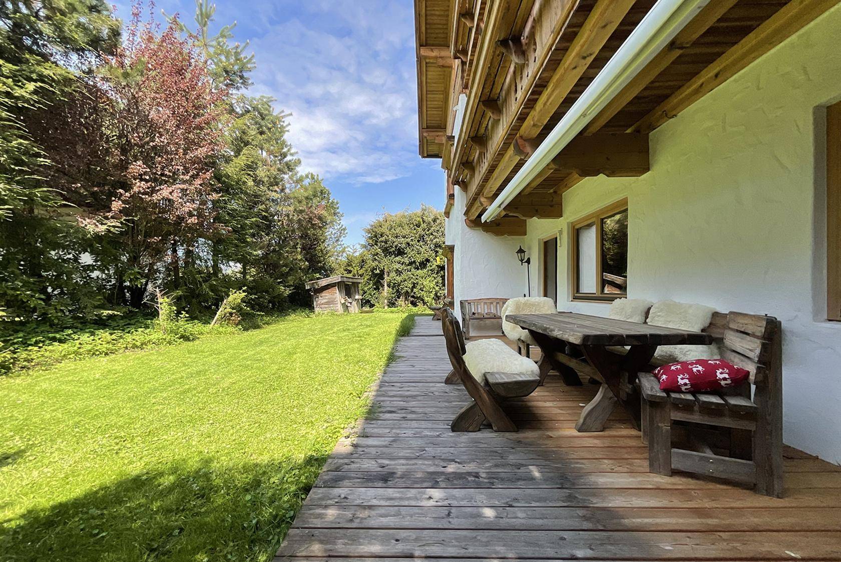 Holzterrasse mit rustikalen Gartenmöbeln und Blick auf den grünen Garten.