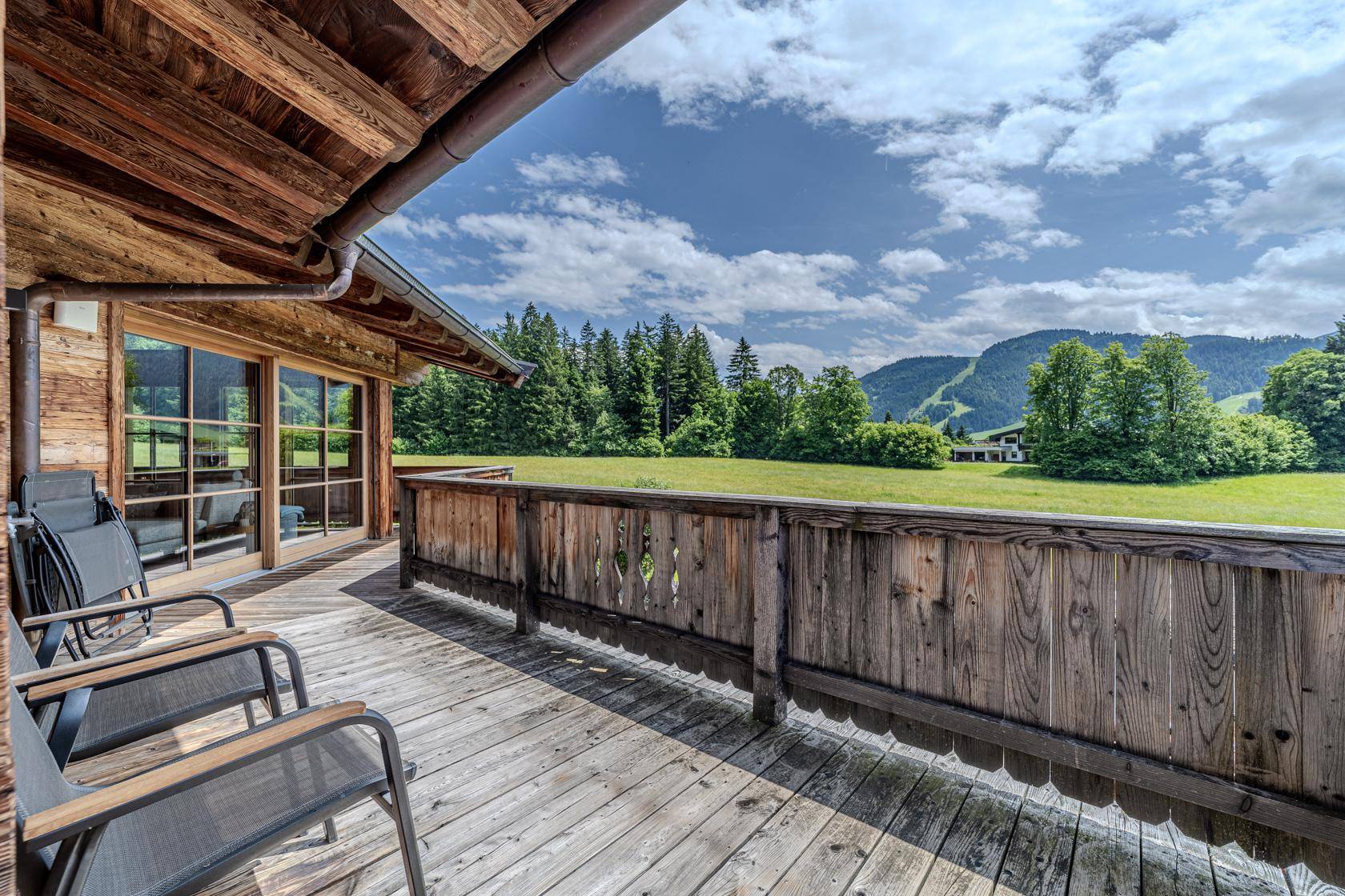 Holzbalkon mit Sitzgelegenheiten und weitem Blick über grüne Wiesen und Wälder.