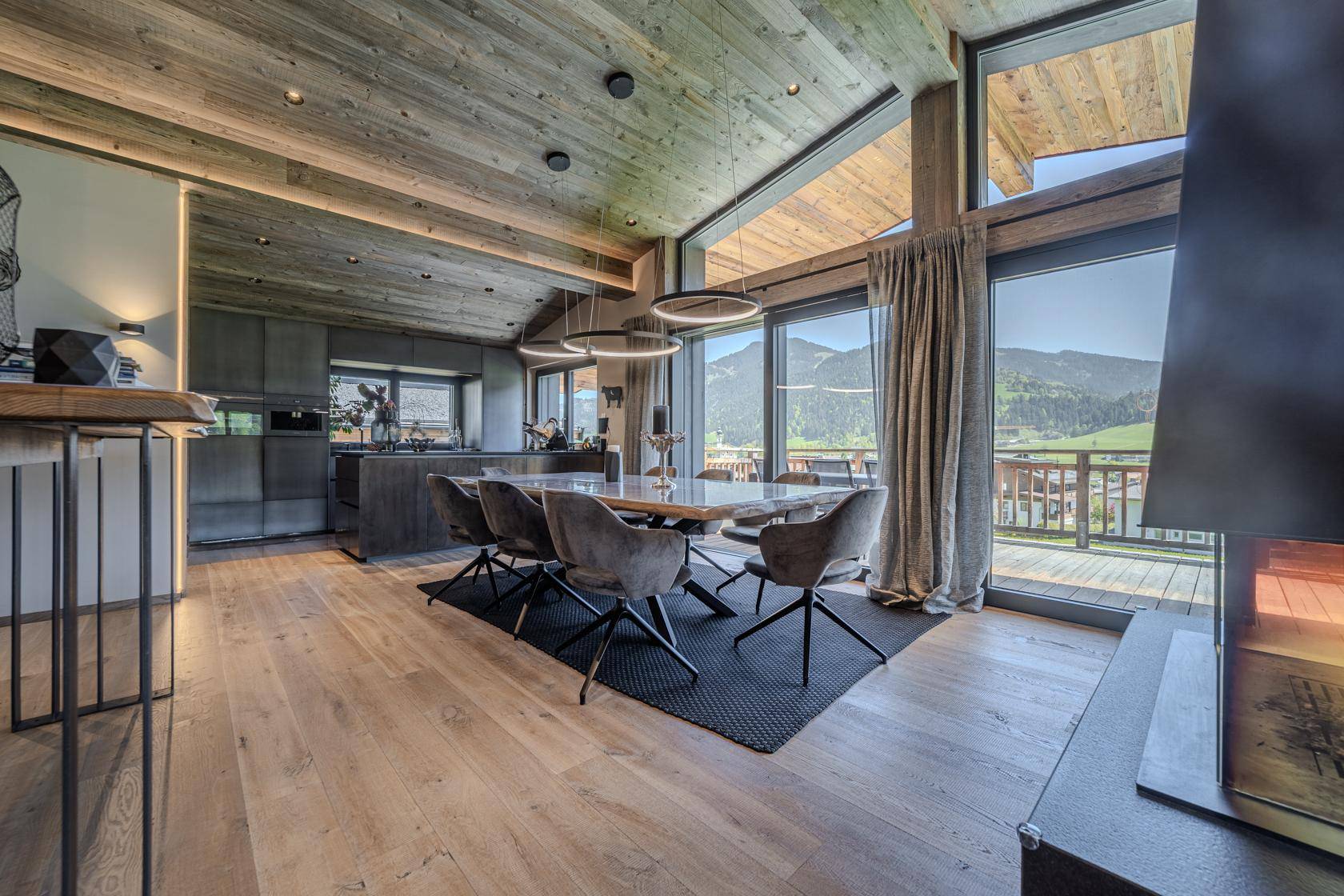Offener Wohn- und Essbereich mit moderner Küche, Holzboden und Panoramafenstern mit Bergblick.