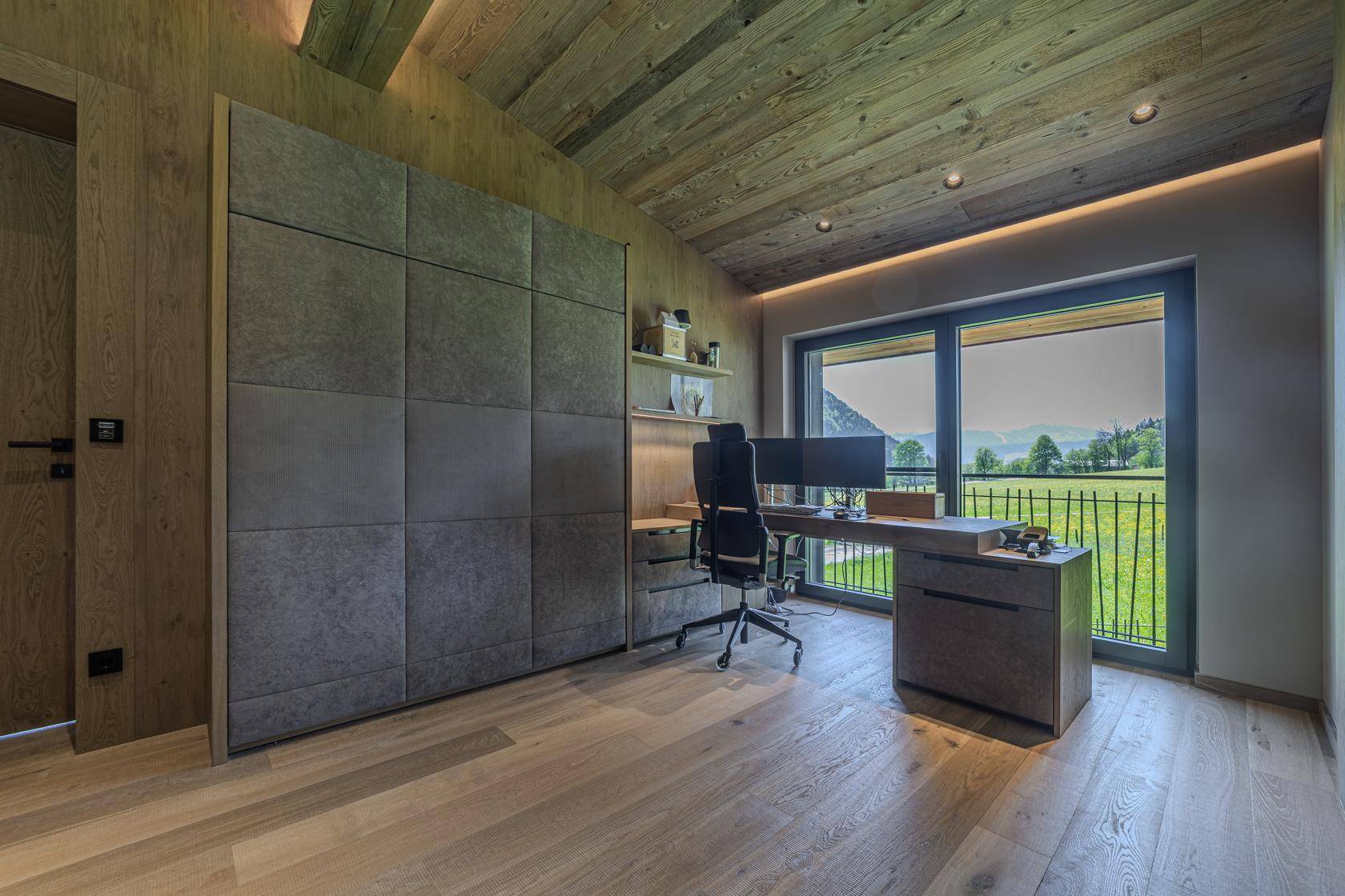 Helles Arbeitszimmer mit Schreibtisch, Einbauschrank und großem Fenster mit Blick ins Grüne.