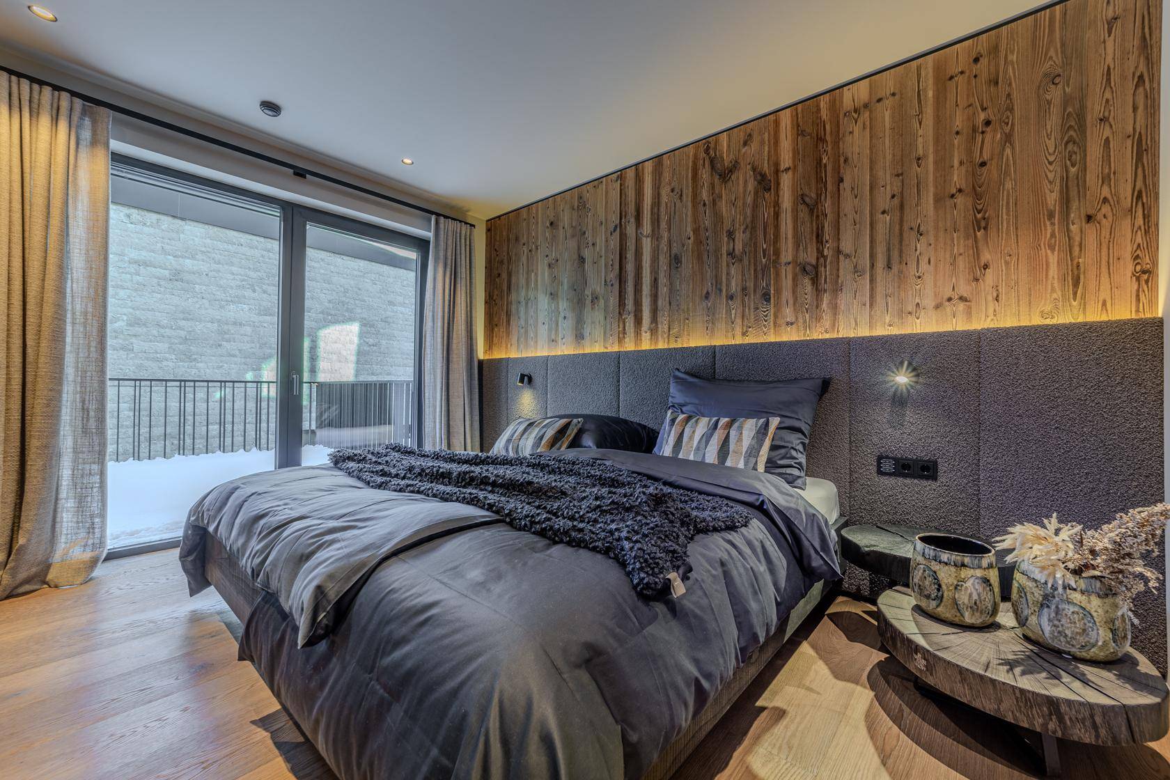 Modernes Schlafzimmer mit Holzwand, großem Bett und Zugang zu einem Balkon.