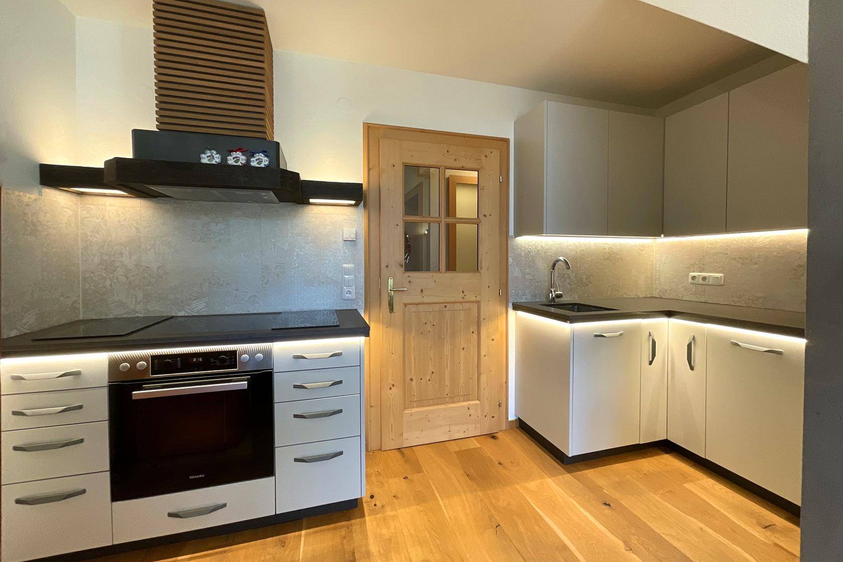 Moderne Küche mit hellgrauen Schränken, Induktionskochfeld, Backofen und Holzboden.