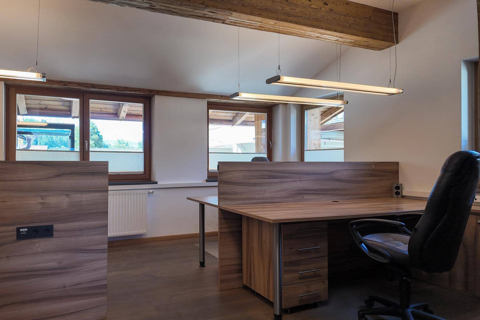 Modernes Büro mit mehreren Arbeitsplätzen, Holzmöbeln und großen Fenstern für viel Tageslicht.