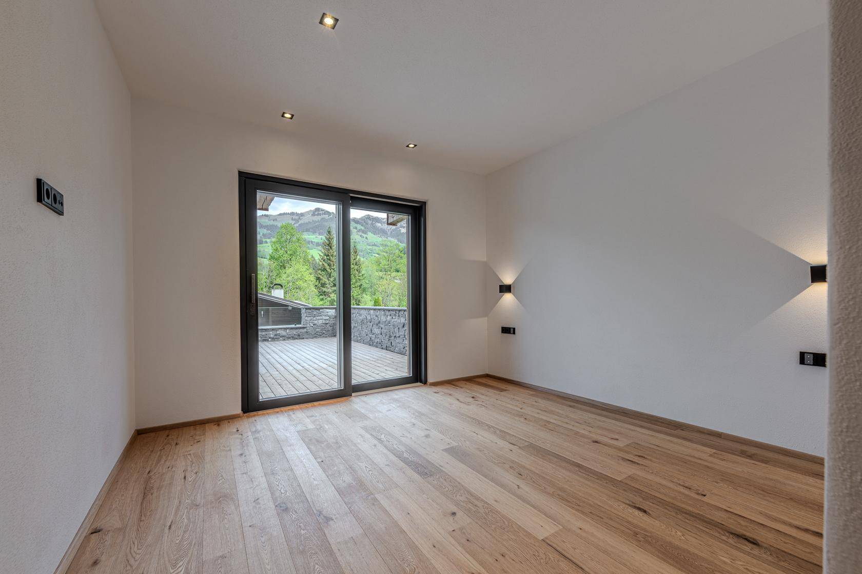 Geräumiges Schlafzimmer mit Holzboden und Zugang zur Terrasse, umgeben von Natur.