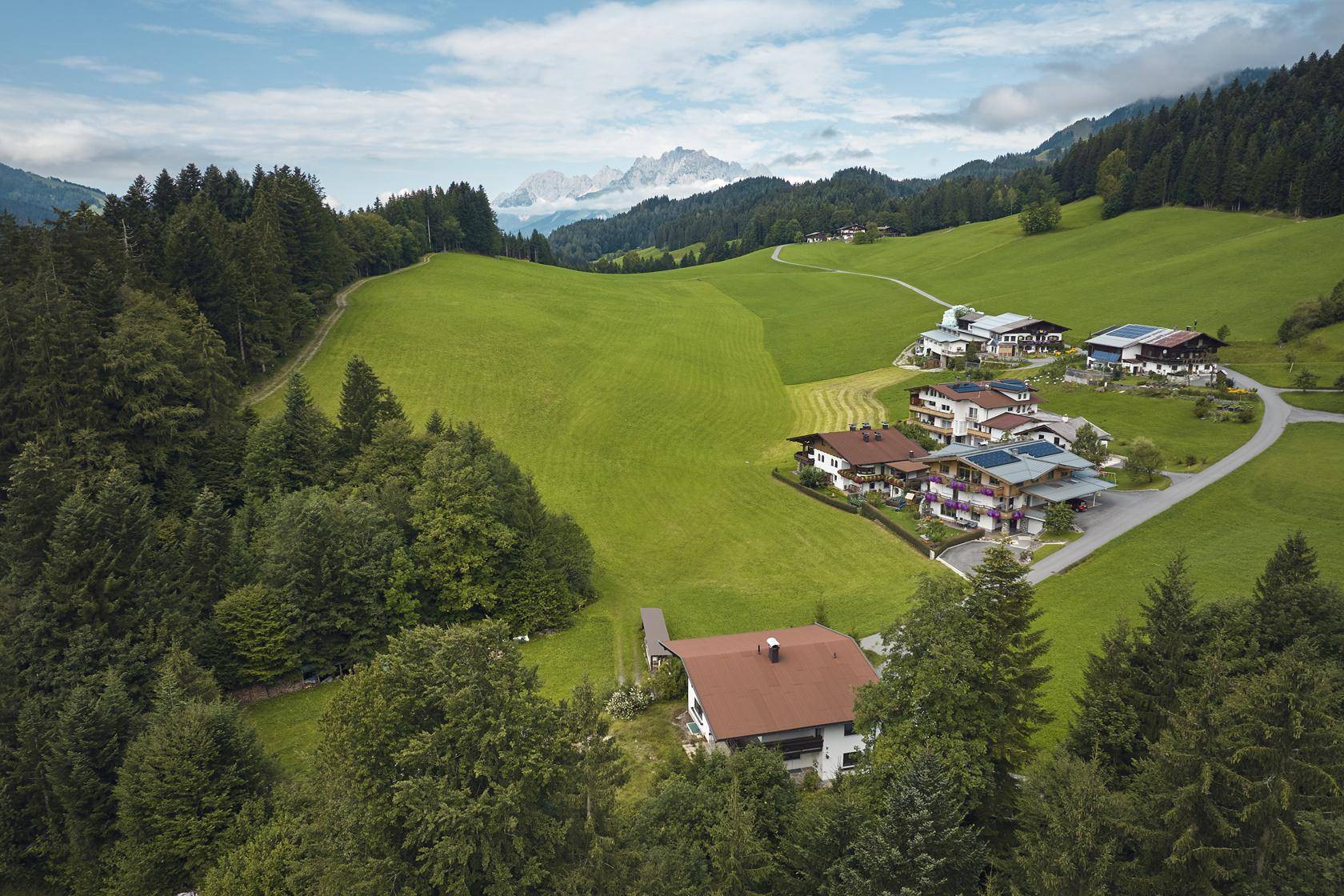 Panoramablick auf ein Dorf in einem grünen Tal, umgeben von Wäldern und majestätischen Bergen.
