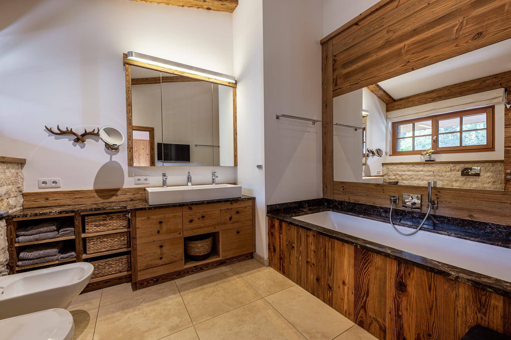 Modernes Badezimmer mit Doppelwaschbecken, Badewanne und Holzelementen im alpinen Stil.