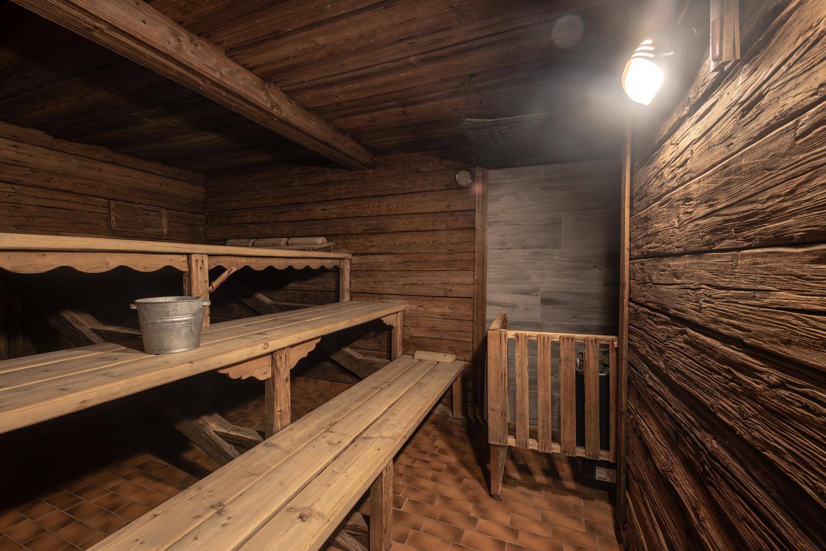 Traditionelle Holzsauna mit mehreren Bänken und Eimer für Aufgüsse.