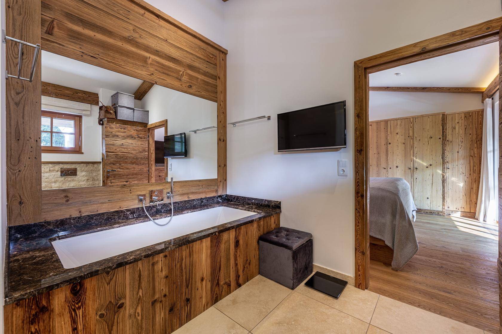 Geräumiges Badezimmer mit Badewanne, Holzelementen und Blick auf das angrenzende Schlafzimmer.
