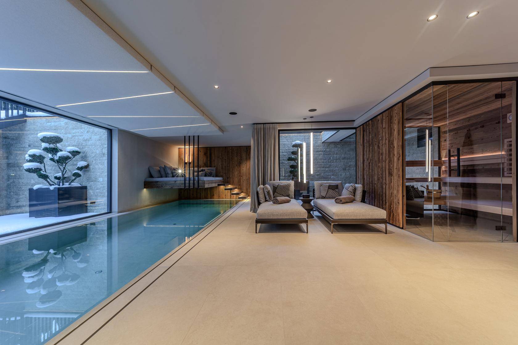 Exklusiver Wellnessbereich mit Innenpool, Liegen und Sauna, umgeben von großen Glasflächen.