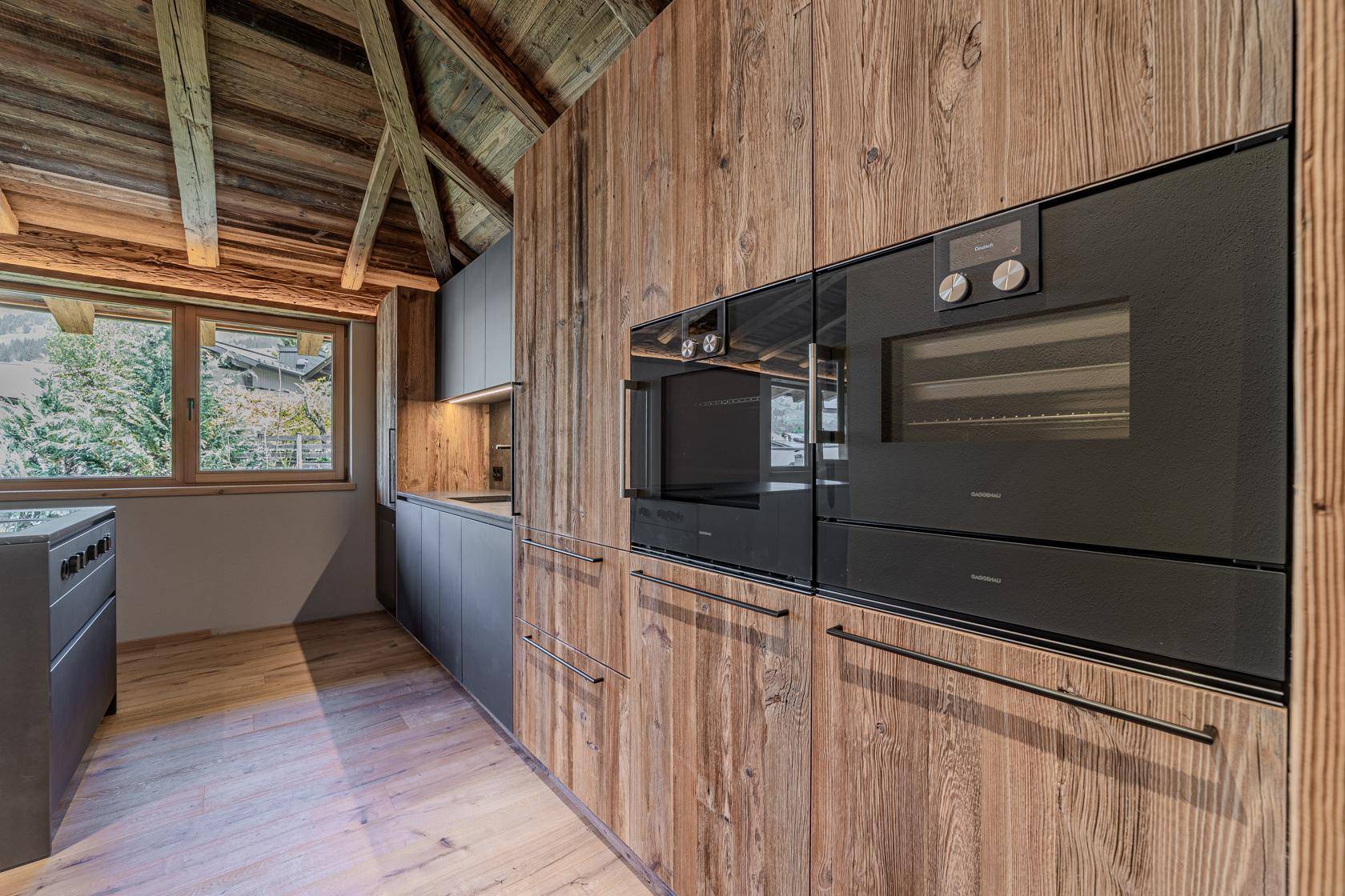 Integrierte Küchenzeile mit Holzwänden und modernen schwarzen Einbaugeräten wie Backofen und Mikrowelle.