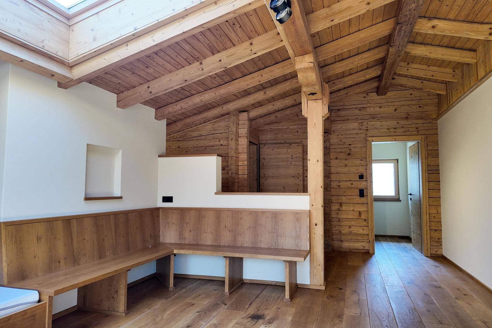 Gemütlicher Wohnbereich im alpinen Stil mit Holzbalkendecke, Einbaubänken und viel natürlichem Licht.