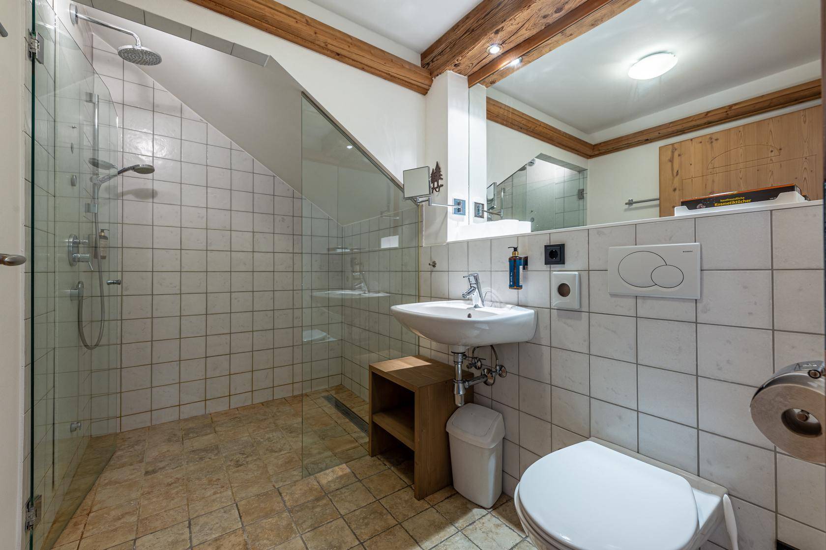 Modernes Badezimmer mit begehbarer Dusche, WC und Waschbecken, akzentuiert durch Holzbalken.