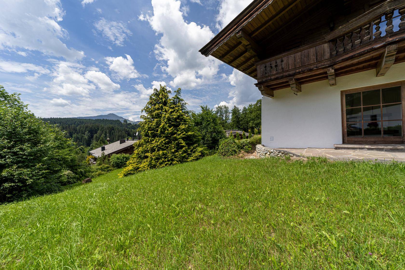 Sonniger Gartenbereich mit Steinterrasse und weitem Blick auf die umliegende Berglandschaft.