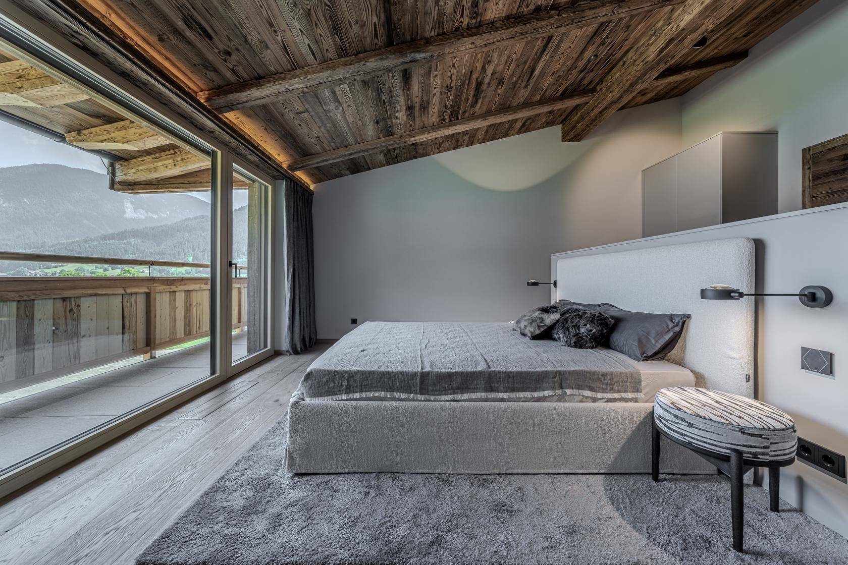 Modernes Schlafzimmer mit Holzbalkendecke, Zugang zum Balkon und Bergblick.