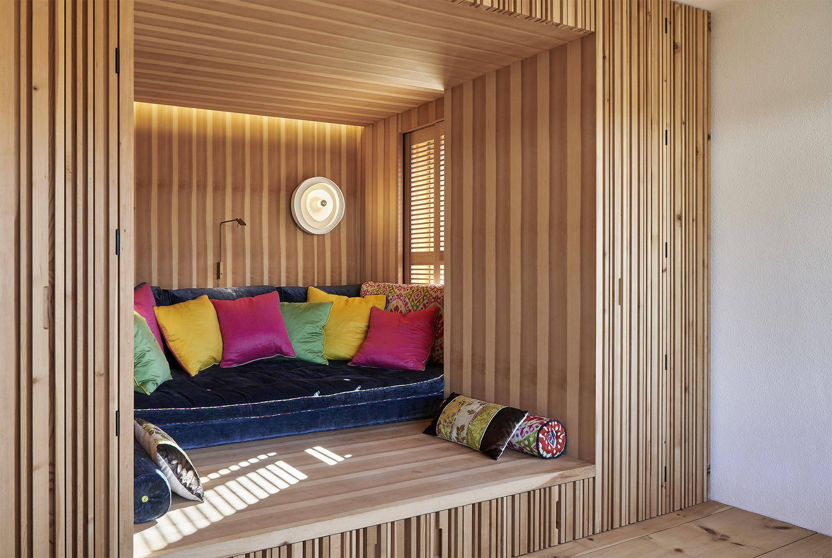 Gemütliche Leseecke mit Holzwänden, bequemer Sitzgelegenheit und farbenfrohen Kissen.