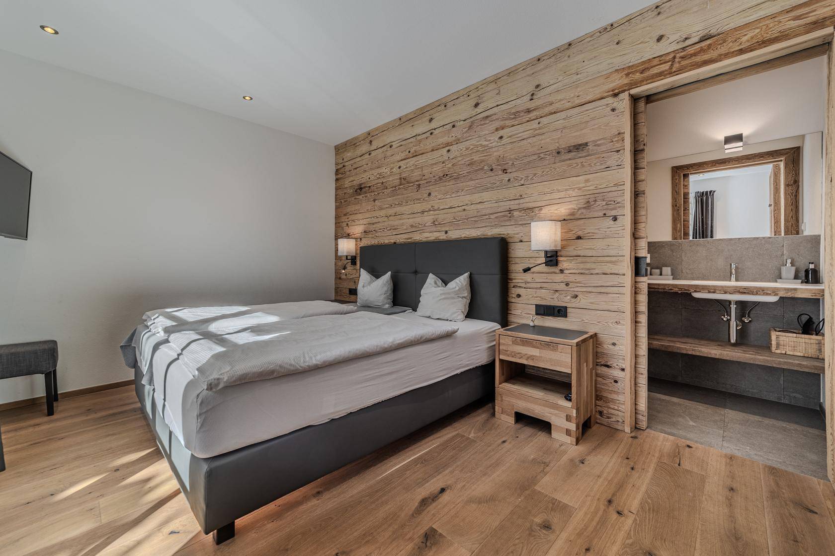 Schlafzimmer mit Holzwand, Holzboden und direktem Zugang zum Badezimmer.