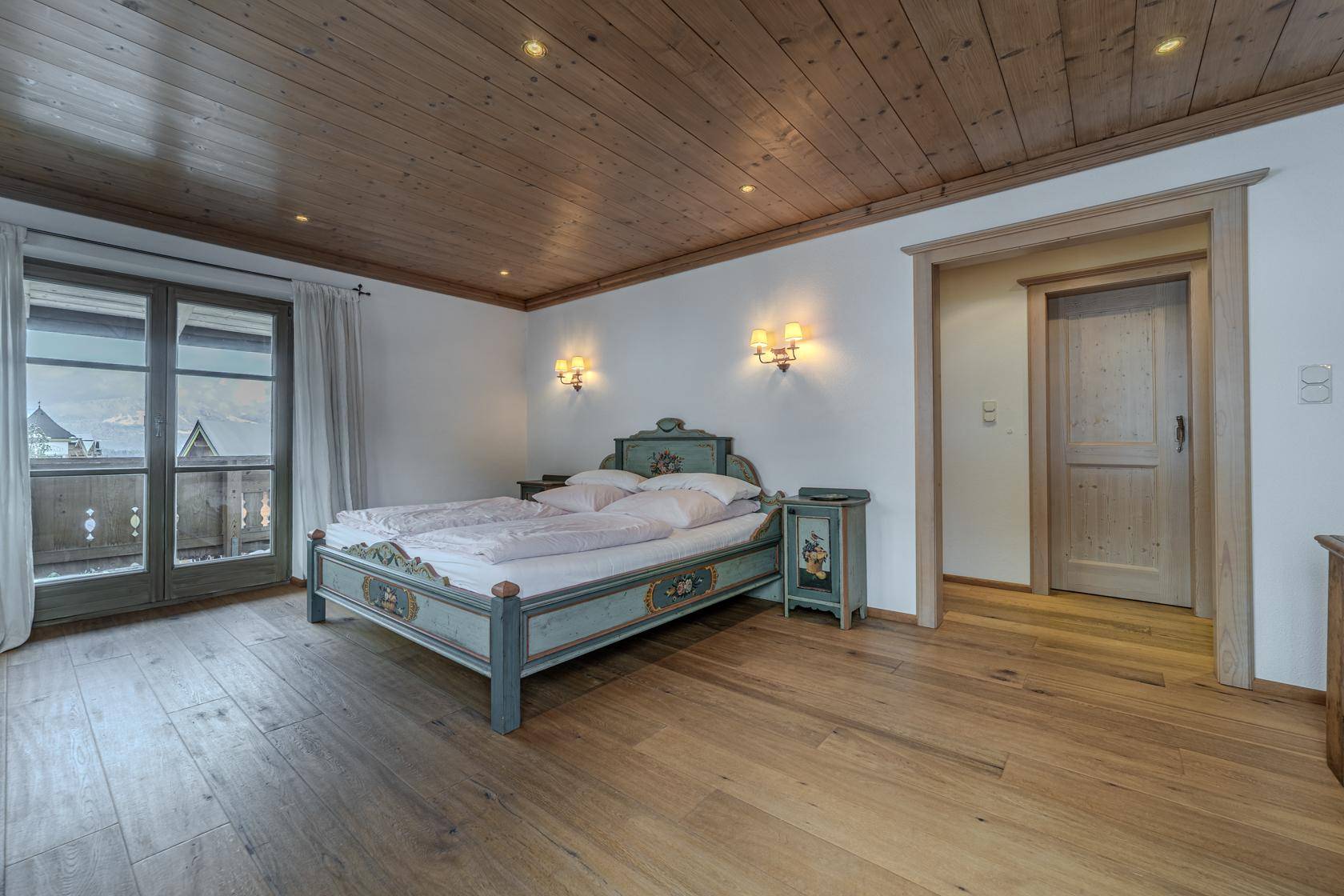 Charmantes Schlafzimmer mit bemaltem Holzbett, Holzboden und direktem Zugang zum Balkon.
