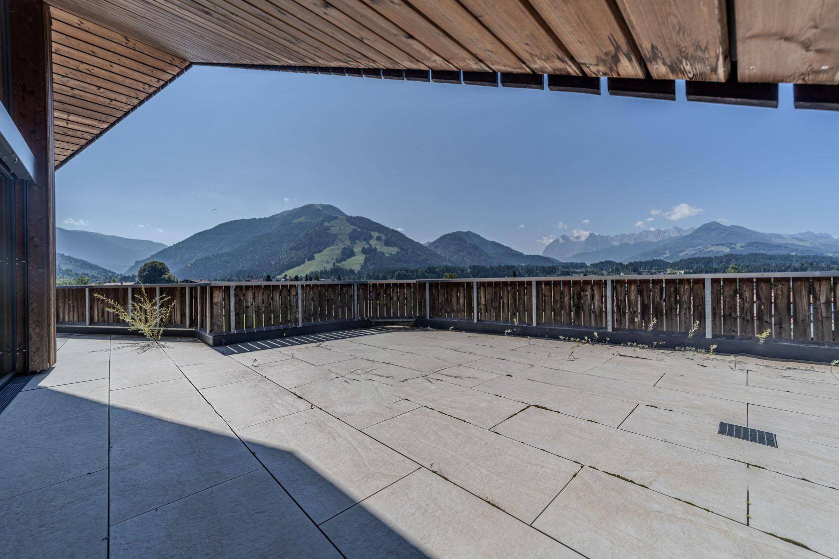 Großzügige Dachterrasse mit Fliesenboden und weitem Blick auf die umliegende Berglandschaft.