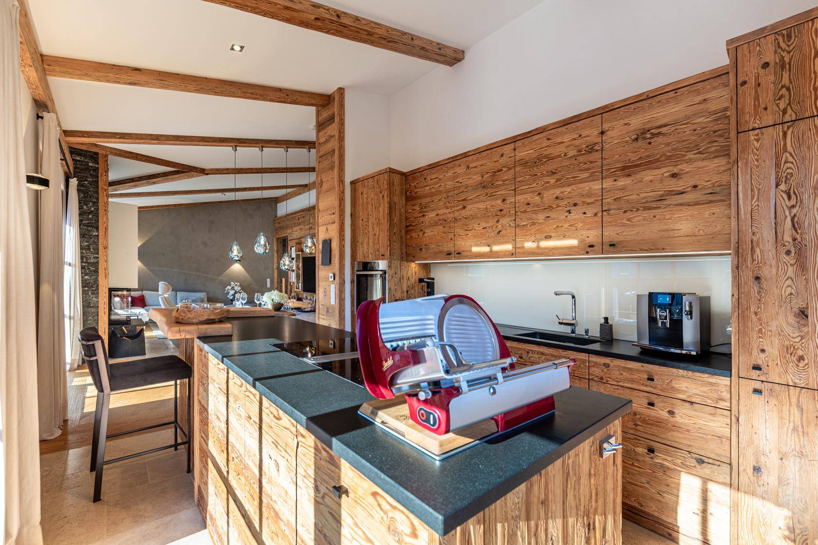 Moderne Holzküche mit Kochinsel, dunkler Arbeitsplatte und Blick in den Wohnbereich.