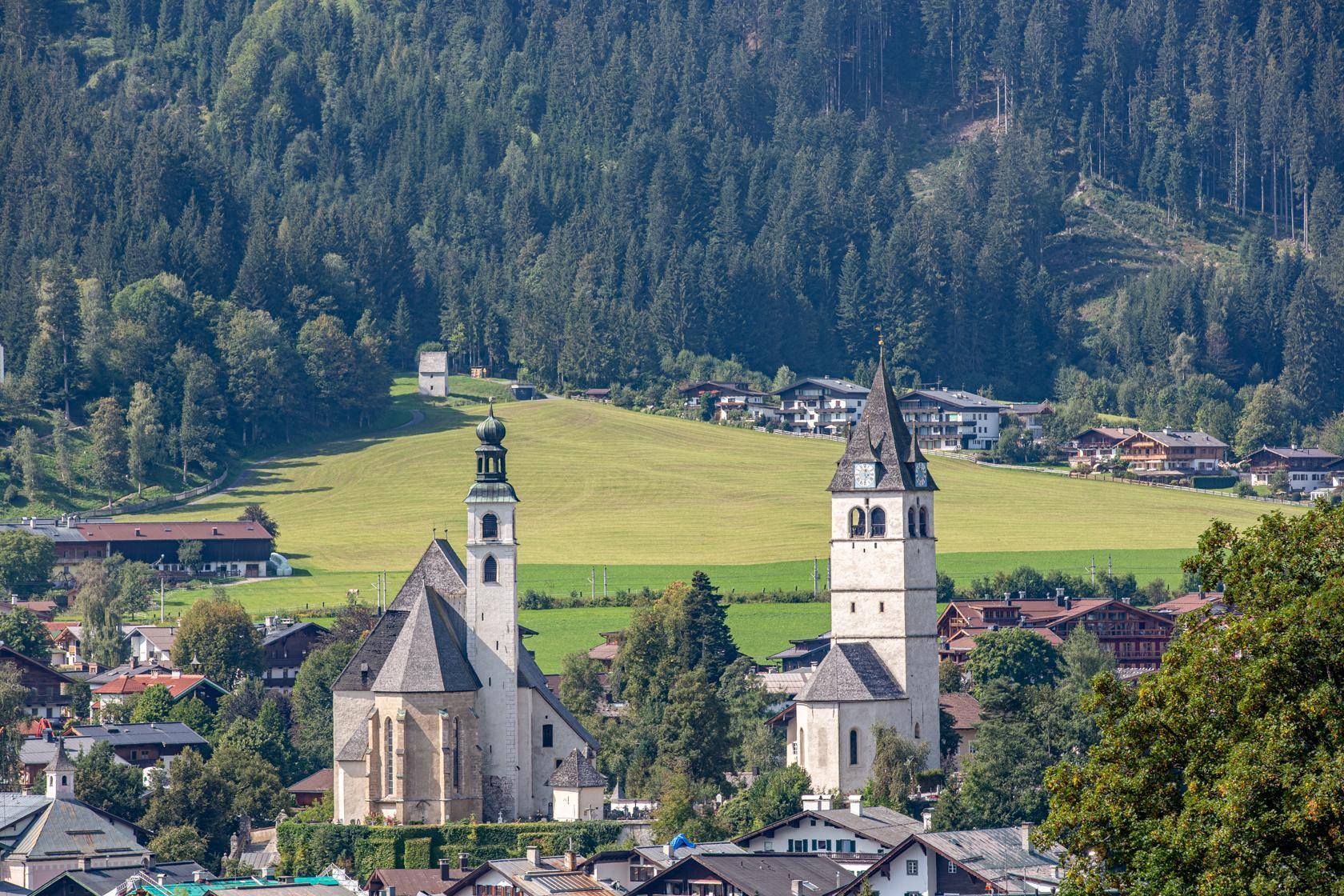 Idyllische Sommerlandschaft mit zwei historischen Kirchen, grünen Hügeln und einem Dorf im Tal.