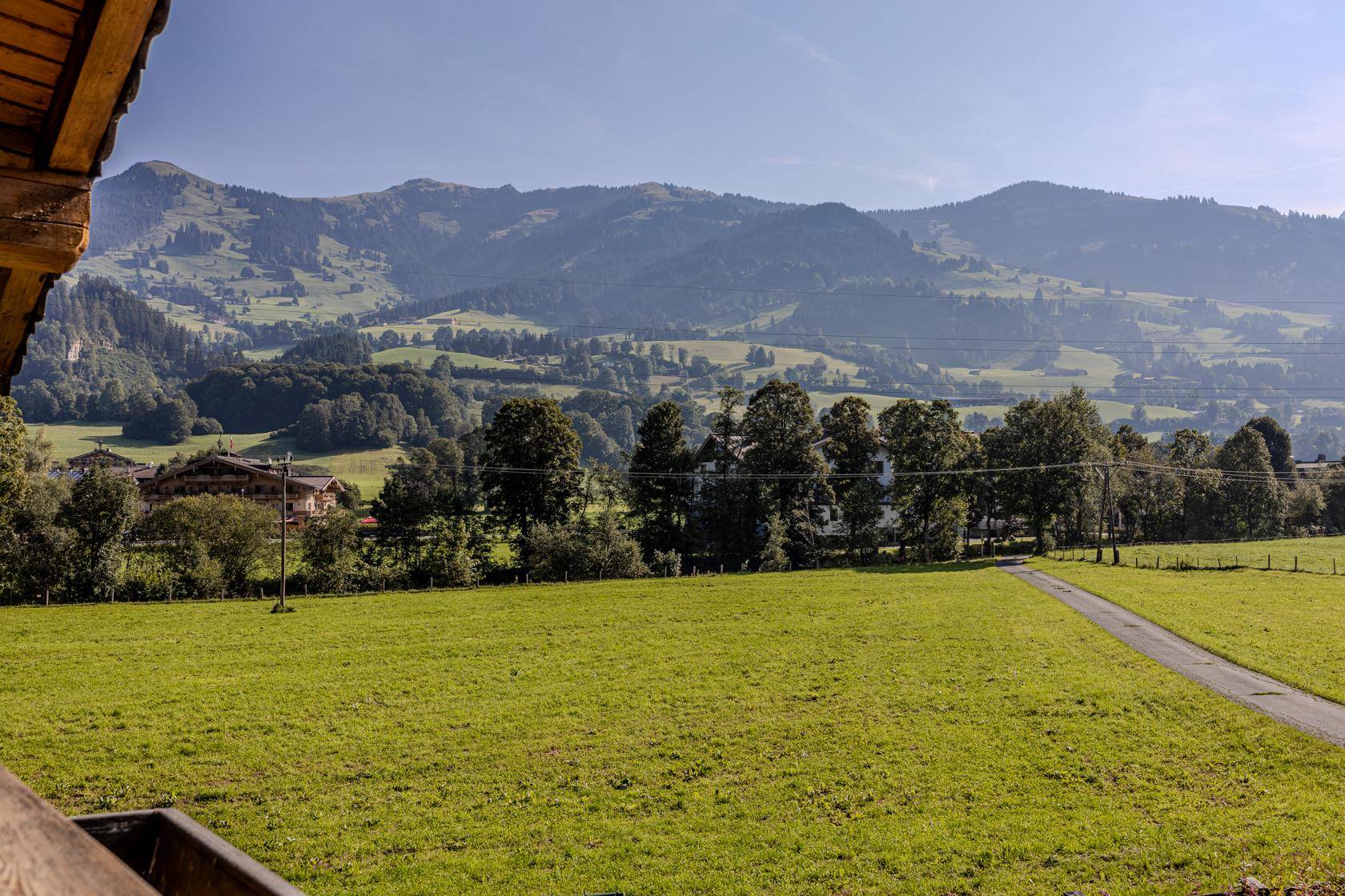 Panoramablick über weite grüne Wiesen und sanfte Hügel mit Bergen im Hintergrund.