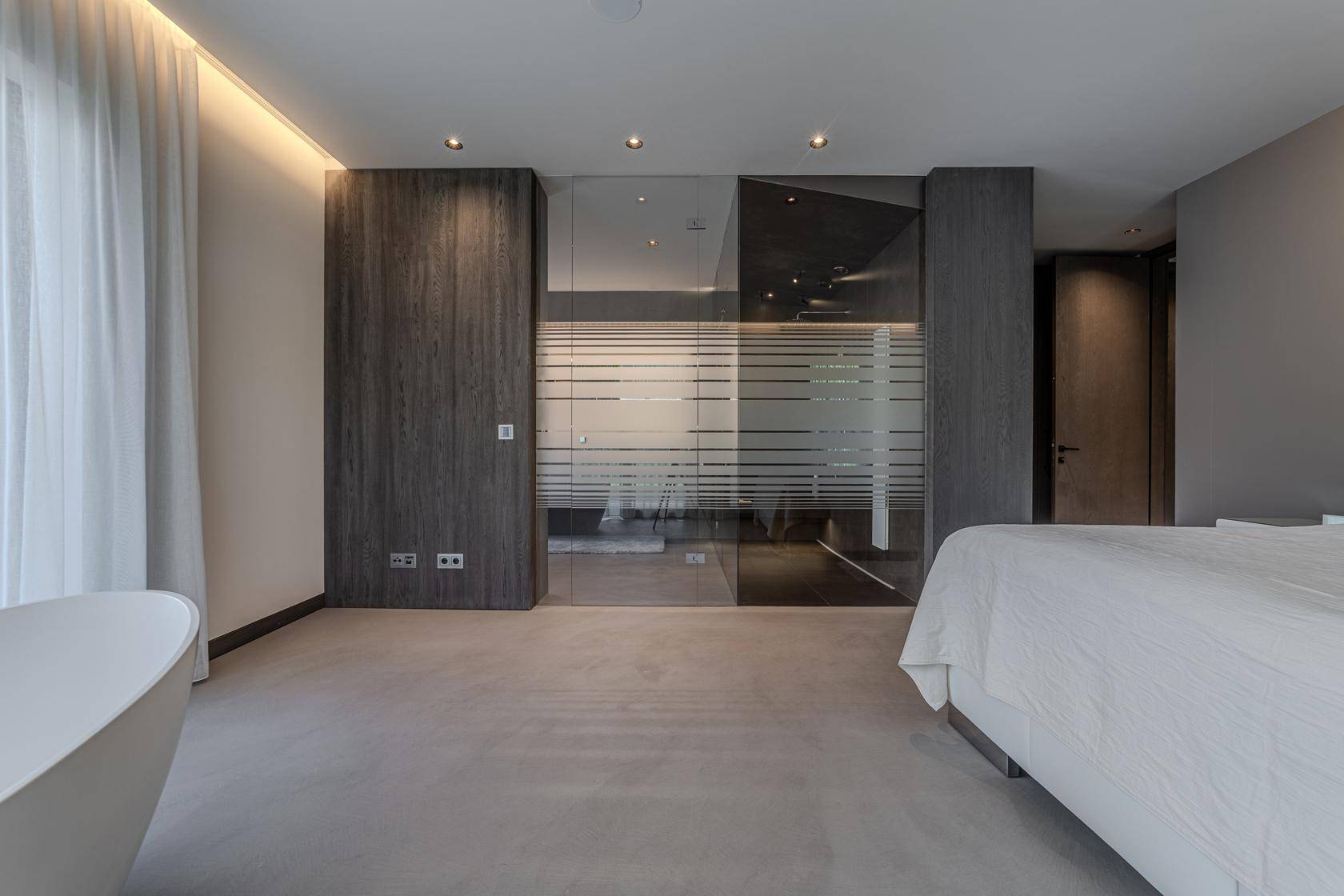 Schlafzimmer mit integriertem Badbereich, freistehender Badewanne und modernen Schränken.