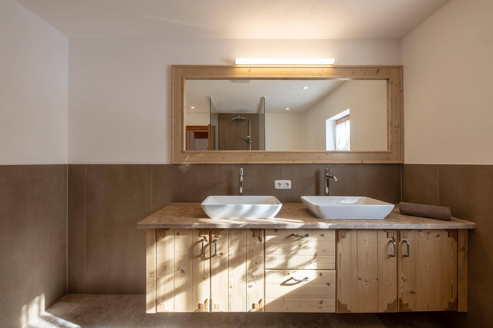 Modernes Badezimmer mit Doppelwaschbecken, Holzunterschrank und großem Spiegel.