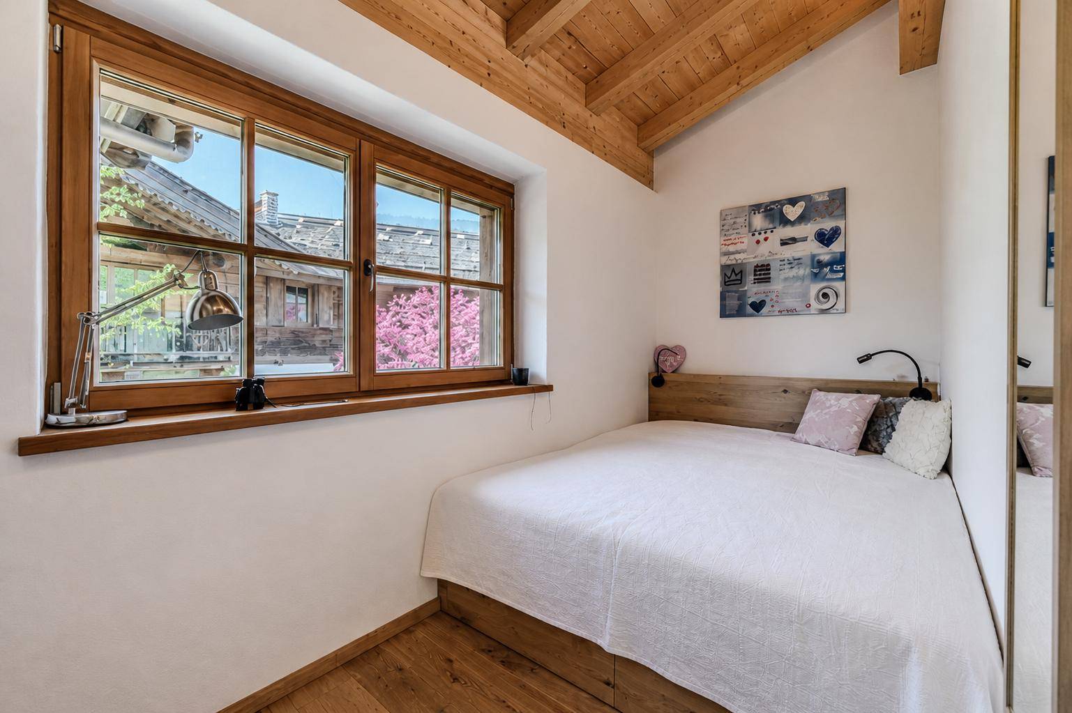 Helles Schlafzimmer mit Holzbalkendecke, Holzboden und großem Fenster mit Ausblick.